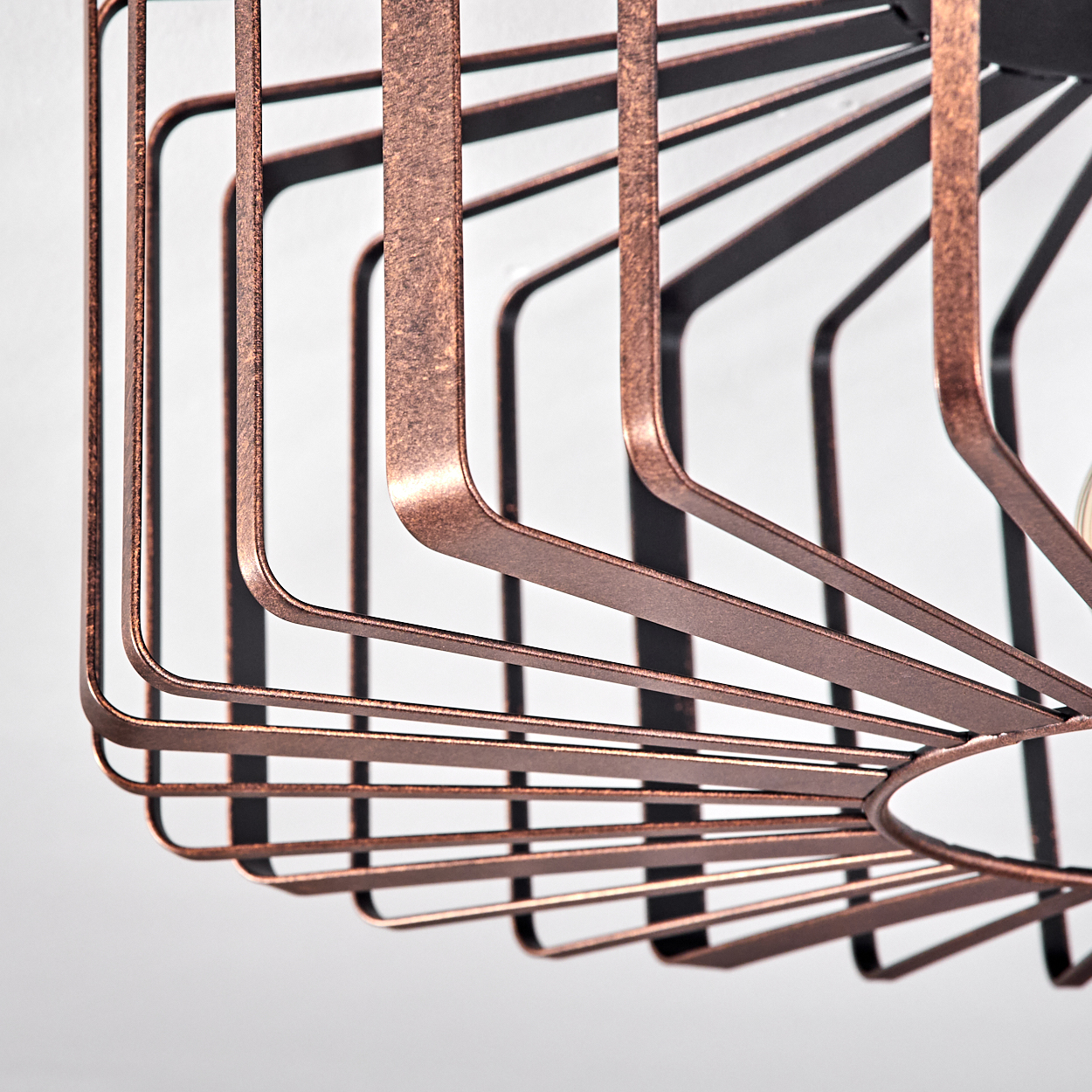 Nahaufnahme eines kupferfarbenen Lampenschirms aus Metall. Das Design hat eine käfigartige Struktur mit gebogenen Linien und weißem Hintergrund.