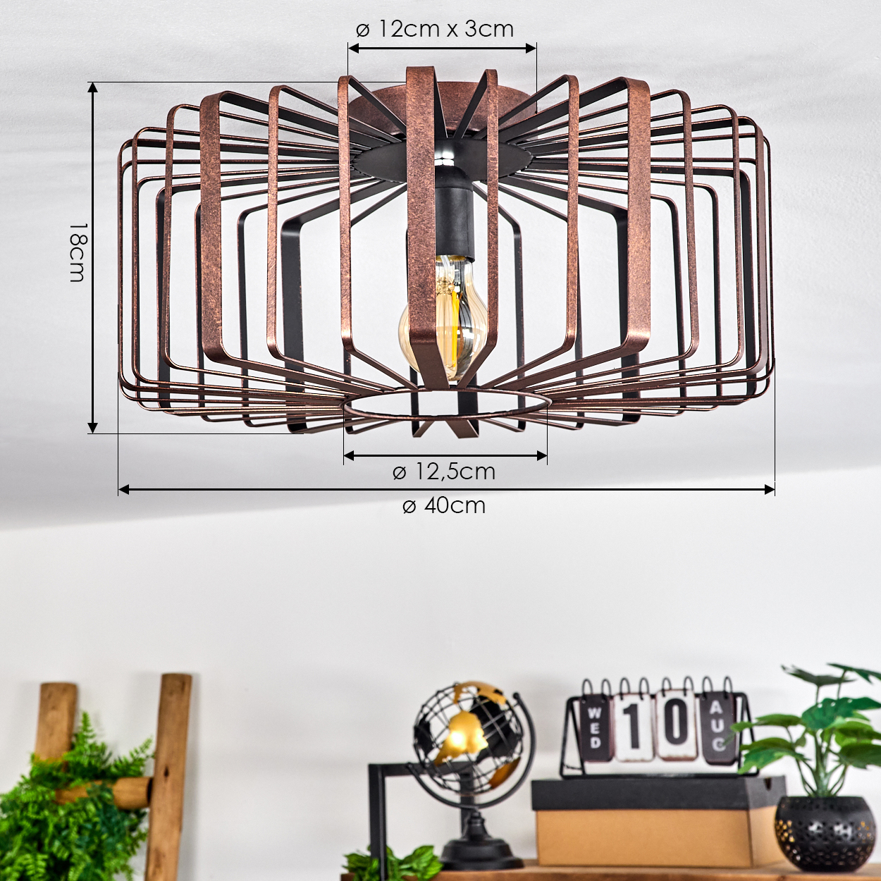 Eine bronzefarbene Drahtrahmen-Deckenleuchte mit freiliegender Glühbirne. Maße sind angegeben. Ein Schreibtisch mit Dekoration befindet sich unter der Lampe.