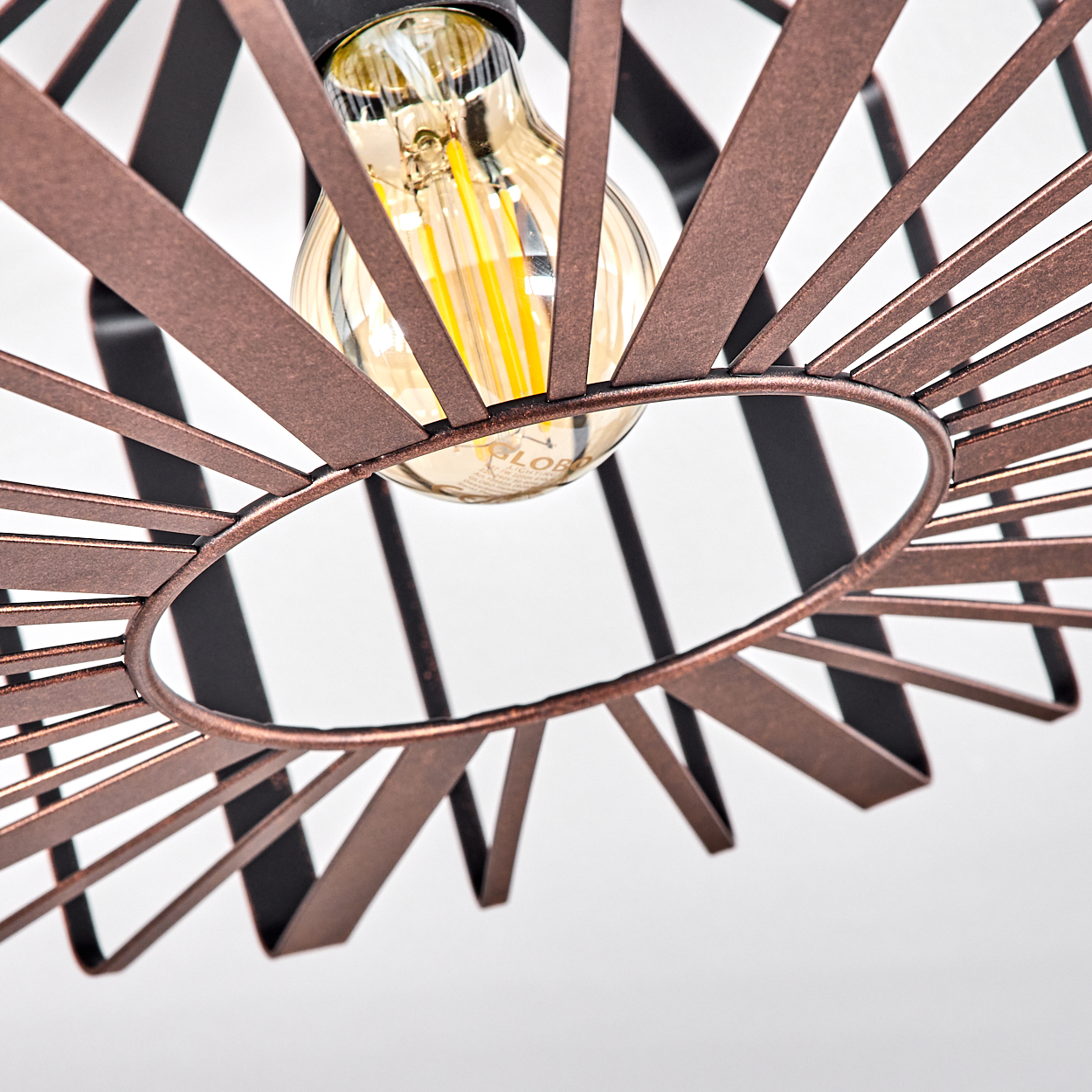 Nahaufnahme eines kupferfarbenen Metalllampenschirms mit einer Glühbirne. Der Lampenschirm hat ein kreisförmiges Design mit radialen Metallstreifen.