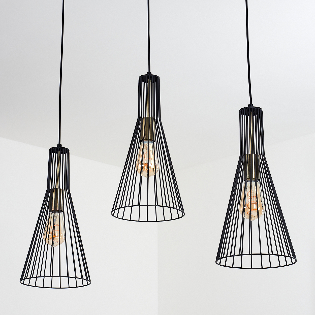 Drei schwarze Pendelleuchten mit Edison-Glühbirnen hängen vor einem weißen Hintergrund. Die Leuchten sind kegelförmig mit Metallrahmen.