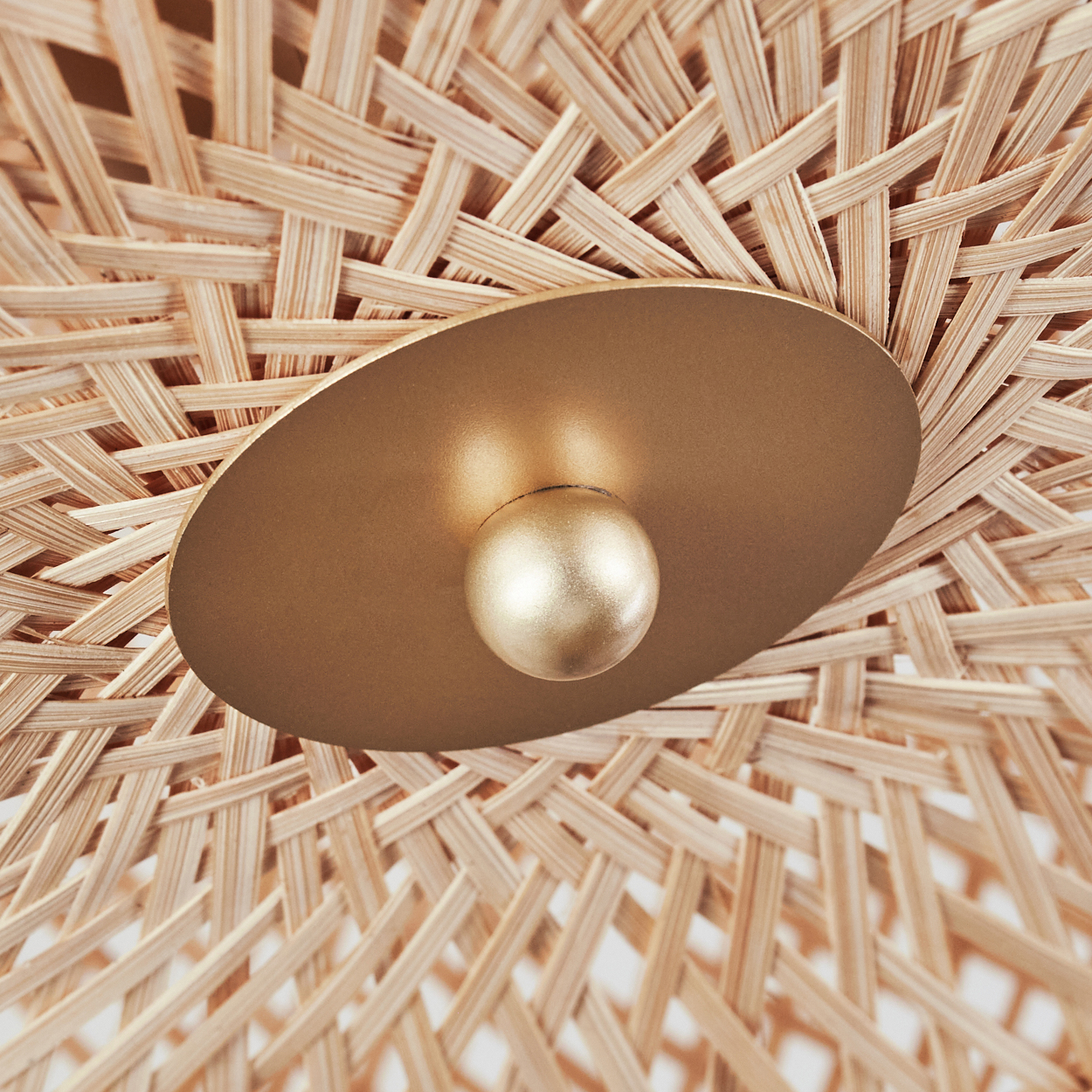 Nahaufnahme einer gewebten Bambuslampe. Eine goldfarbene, runde Leuchte sitzt auf einem gewebten Bambussockel. Die Lampe hat eine goldene Glühbirne.