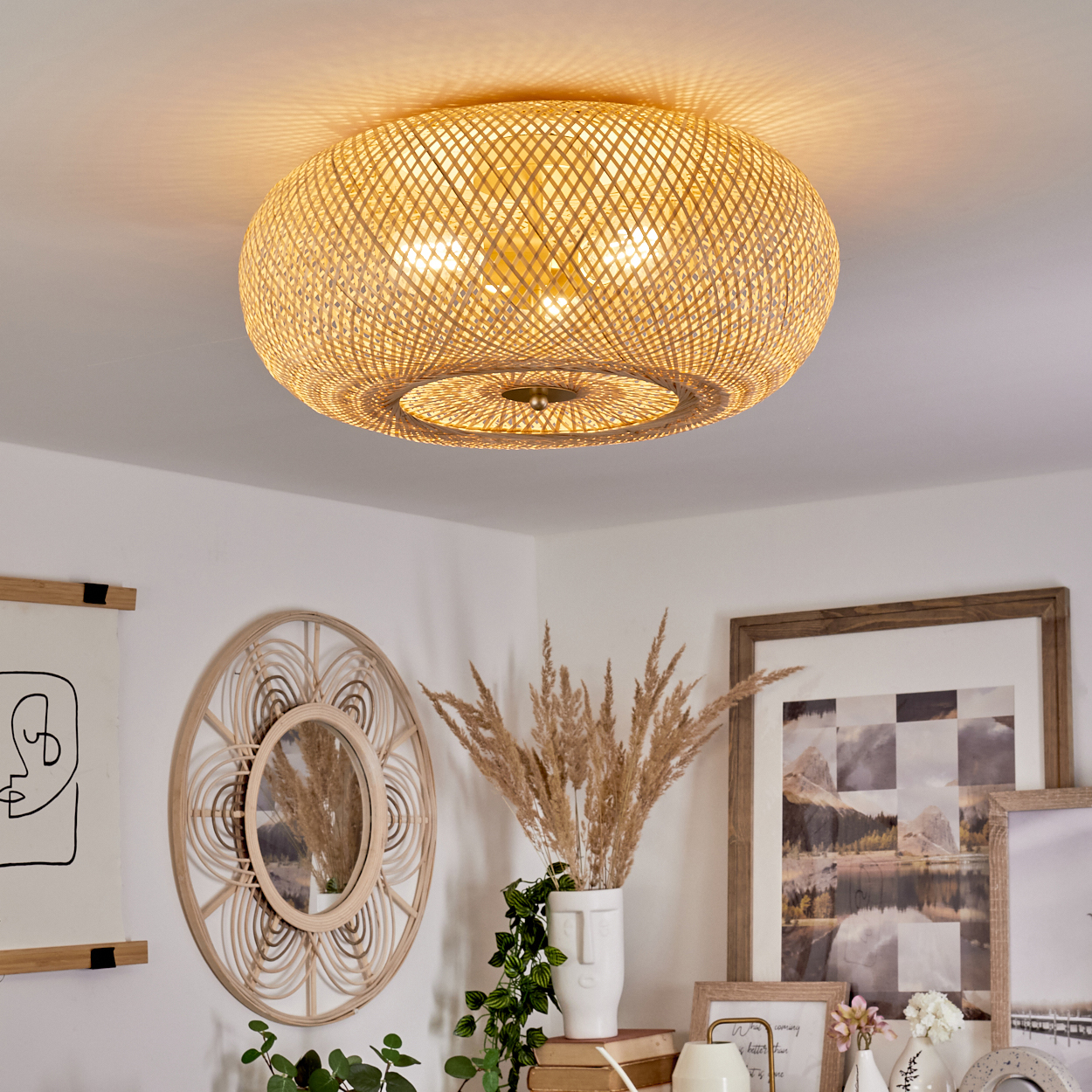 Eine Deckenlampe aus Rattan beleuchtet einen Raum. Darunter sind ein Spiegel, Kunstwerke und eine Vase mit getrockneten Pflanzen zu sehen.