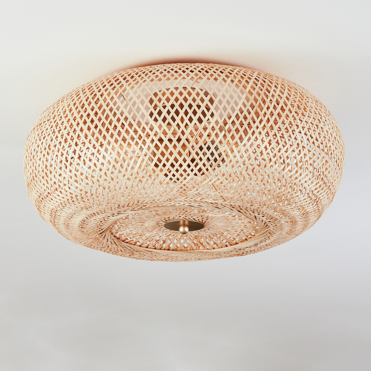 Eine Deckenlampe aus geflochtenem Rattan ist an einer weißen Decke befestigt. Die Lampe hat eine kugelförmige Form mit einem zentralen Messingdetail.