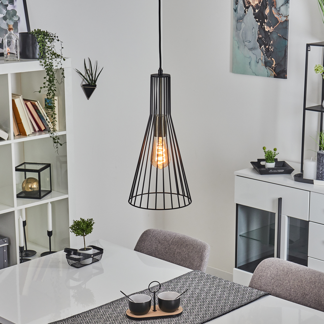 Ein modernes Esszimmer mit weißem Tisch, schwarzem Kronleuchter, Stühlen und Dekorationsartikeln auf Regalen und einem Schrank.