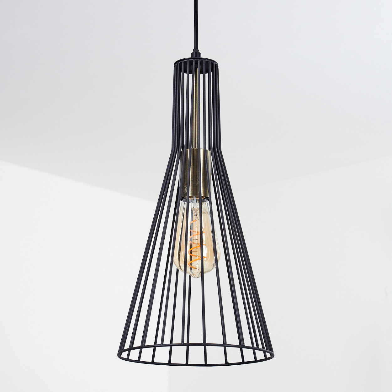 Schwarze Metallkäfig-Pendelleuchte mit goldfarbenem Glühbirnenhalter und warmer, leuchtender Glühbirne auf weißem Hintergrund.