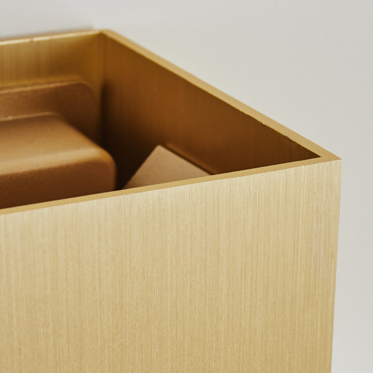Nahaufnahme einer goldenen Box mit strukturierter Oberfläche. Im Inneren befinden sich weitere goldene Objekte unterschiedlicher Form und Größe. Der Hintergrund ist schlicht.