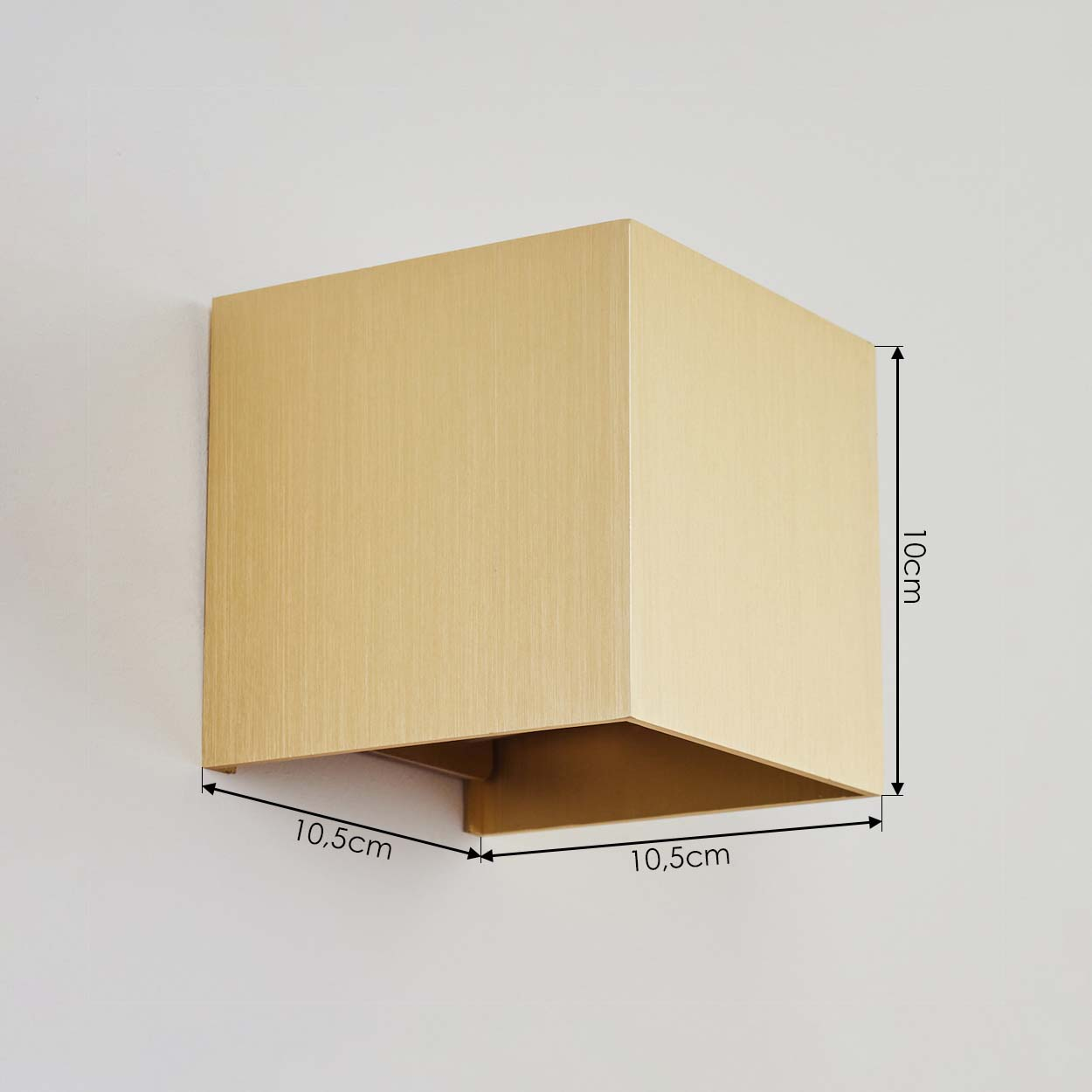 Eine goldene, quadratische Wandleuchte ist an einer weißen Wand montiert. Maße sind beschriftet: 10 cm Höhe, 10,5 cm Breite.