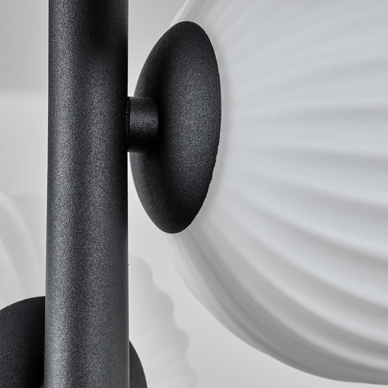 Nahaufnahme einer schwarzen Metalllampe. Eine schwarze Stange trägt einen weißen, geriffelten, kugelförmigen Schirm. Der Hintergrund ist weiß.