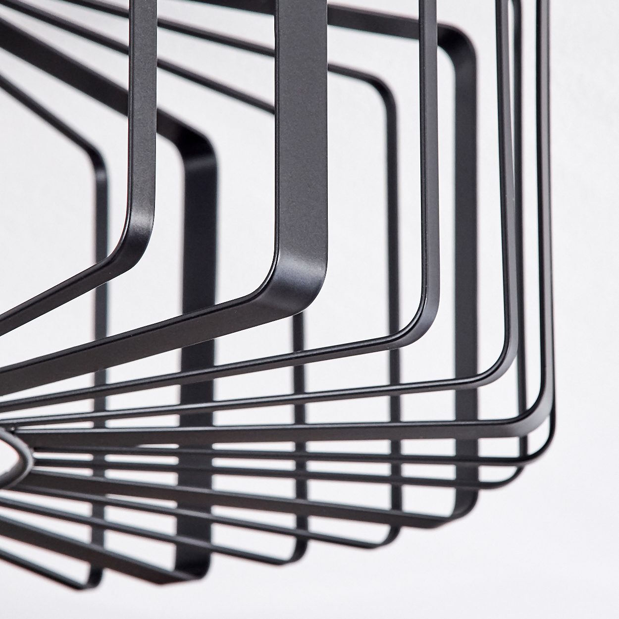 Nahaufnahme eines schwarzen Metallkorbs mit geometrischem Design vor weißem Hintergrund. Die Struktur hat geschwungene Linien und ein käfigartiges Aussehen.
