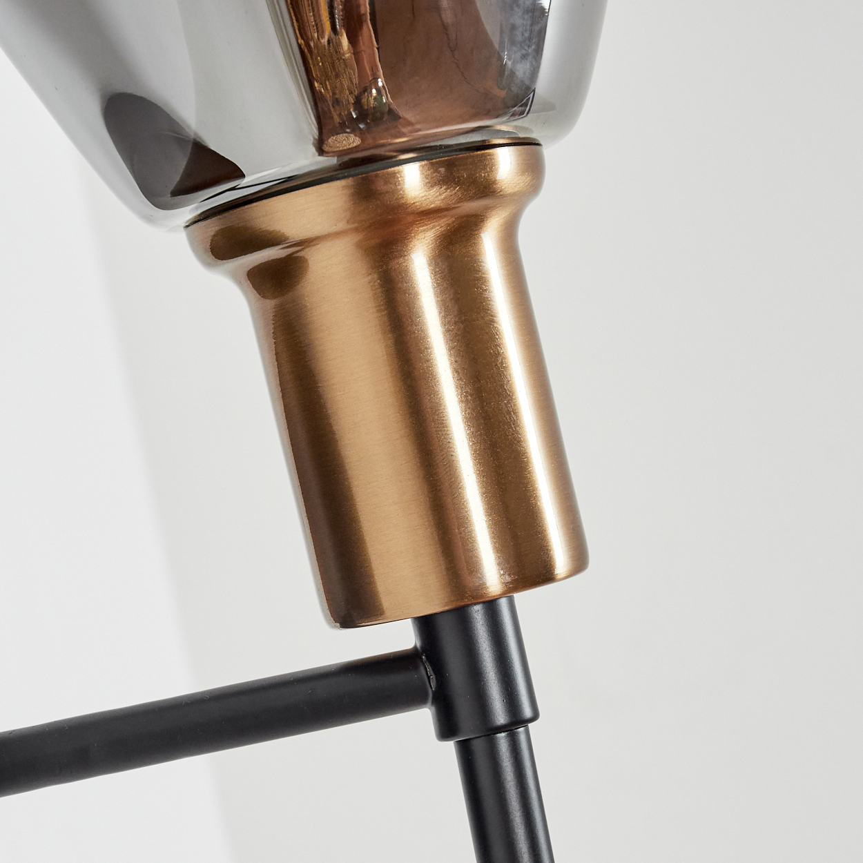 Nahaufnahme einer modernen Lampe. Sie hat einen bronzefarbenen Sockel, einen schwarzen Stiel und einen dunklen Glasschirm. Der Hintergrund ist weiß.