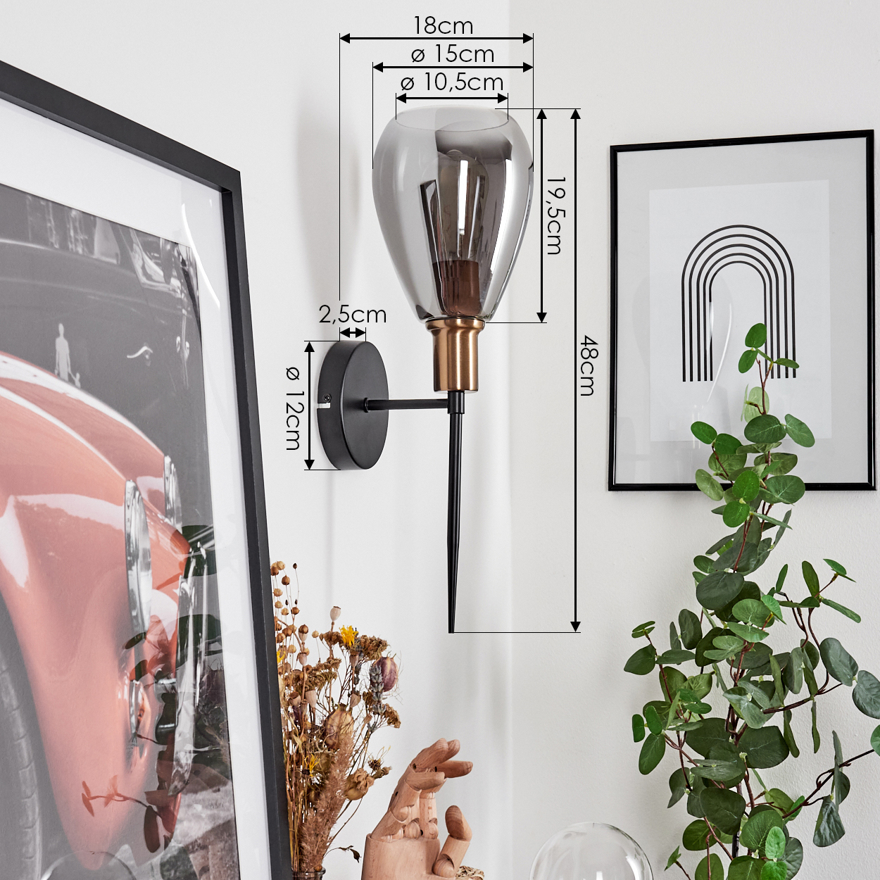 Wandlampe mit Maßen, gerahmter Kunst und Grünpflanzen. Die Lampe hat einen rauchigen Glasschirm, Messingakzente und einen schwarzen Stiel.