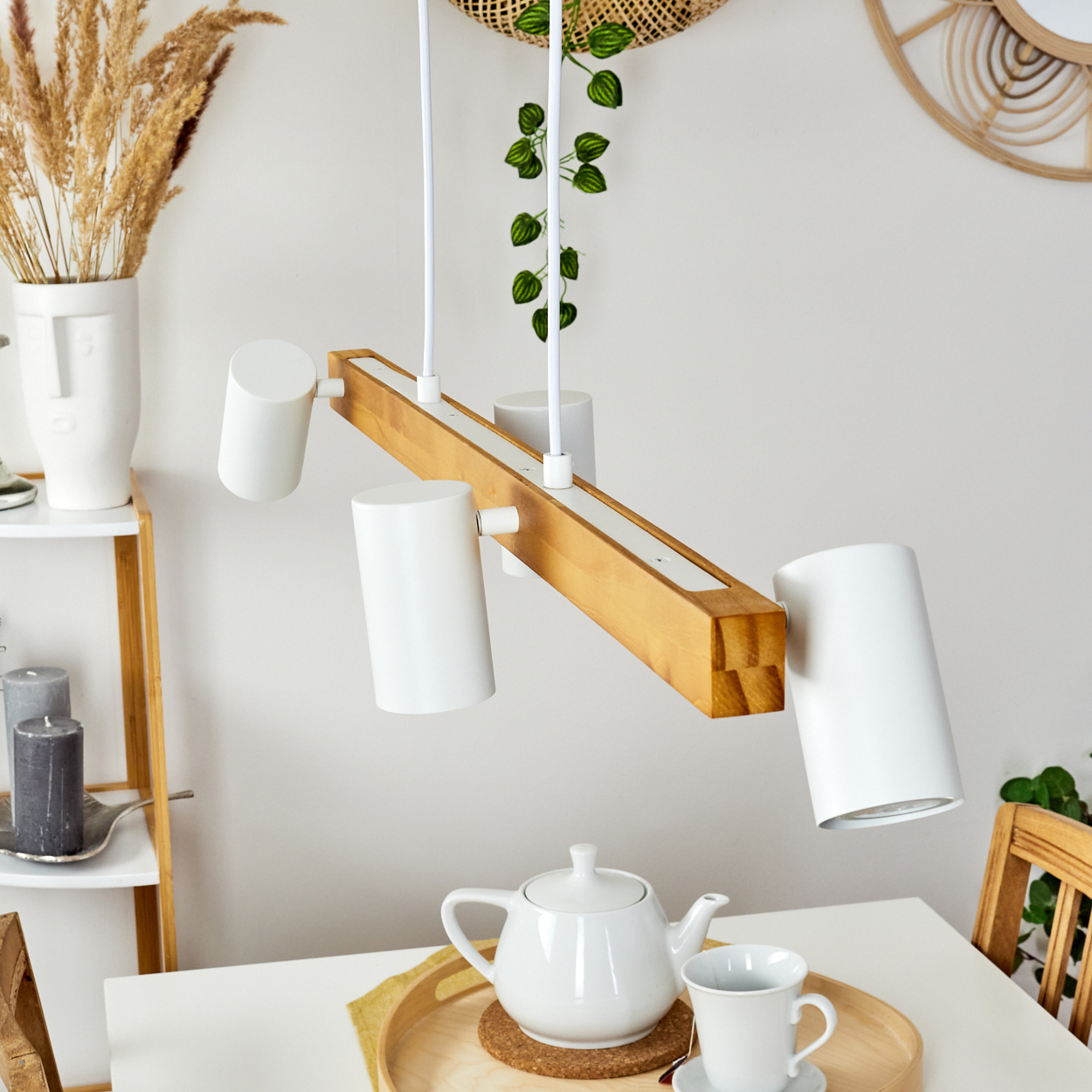 Eine moderne Holz- und Weiß-Lampe hängt über einem Tisch mit Teekanne, Tasse und Tablett. Beige und weiße Dekoration im Hintergrund.