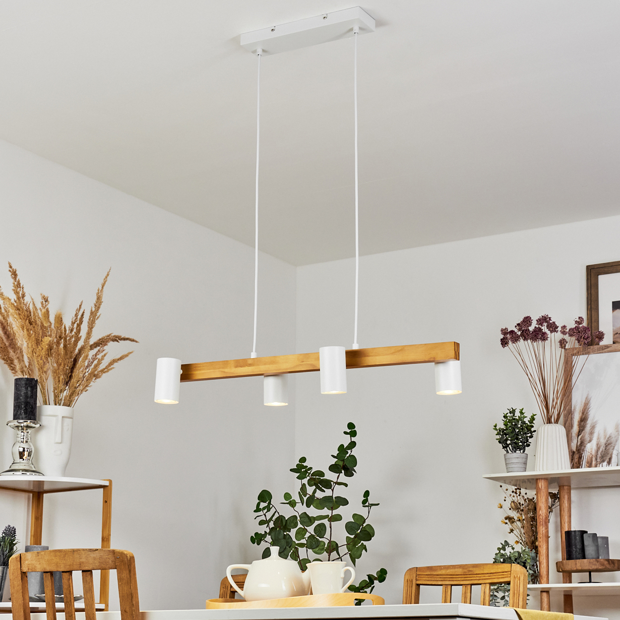 Ein Esszimmer mit Holzbalken-Leuchte, weißen Wänden, Regalen mit Pflanzen und Deko. Ein Tisch ist mit Tee gedeckt.