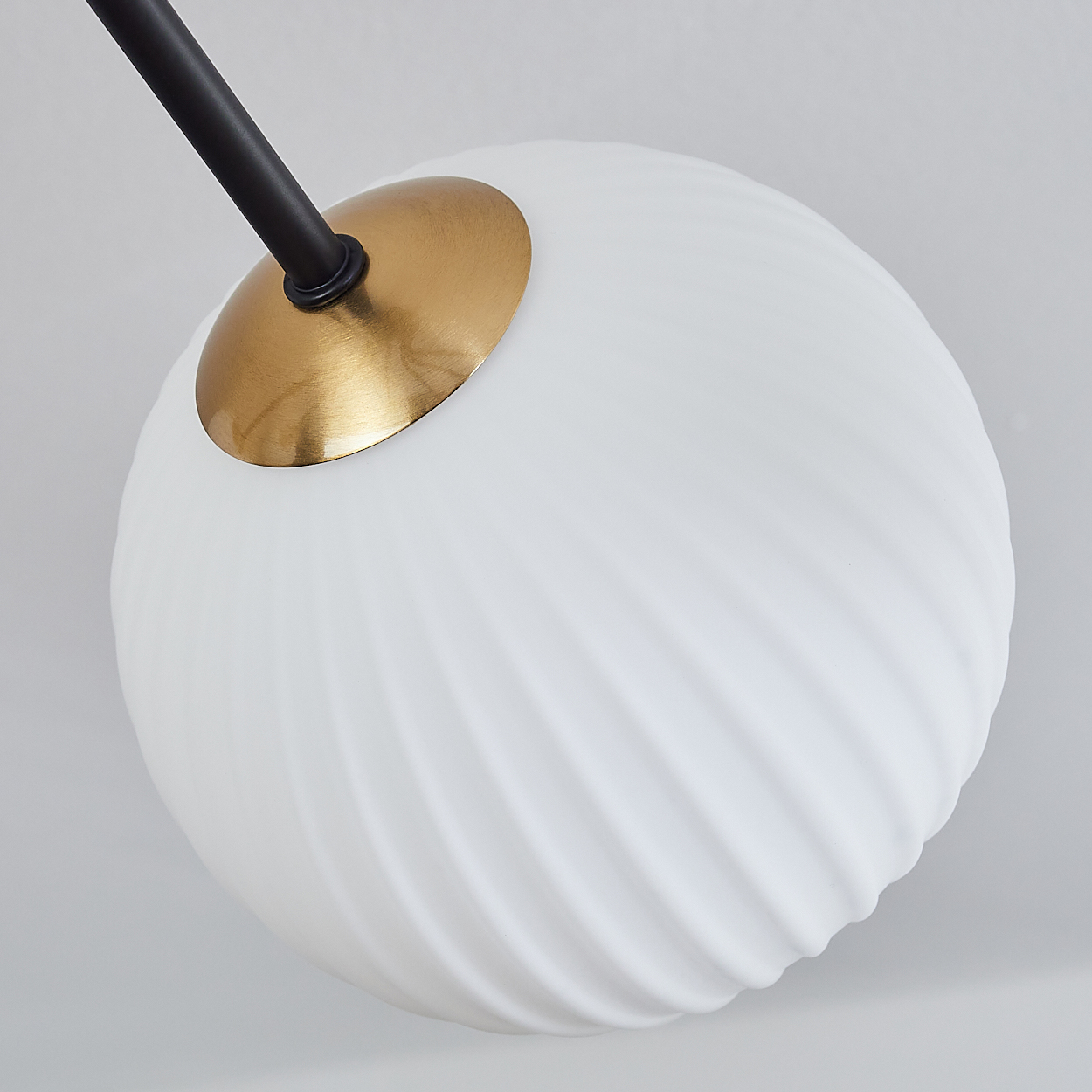 Nahaufnahme einer modernen Lampe. Sie hat eine weiße, gerippte Kugel mit goldenem Sockel und schwarzem Stiel vor weißem Hintergrund.