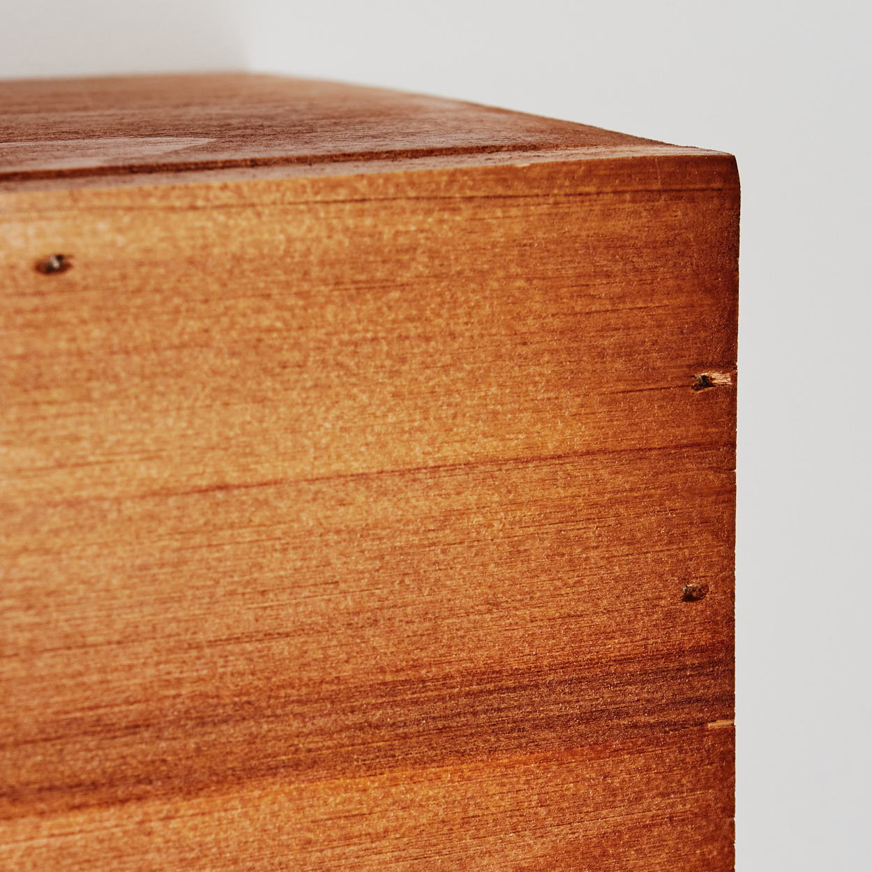 Nahaufnahme einer Holzkistecke. Das Holz ist braun mit sichtbarer Maserung. Kleine Nägel sind sichtbar. Der Hintergrund ist weiß.