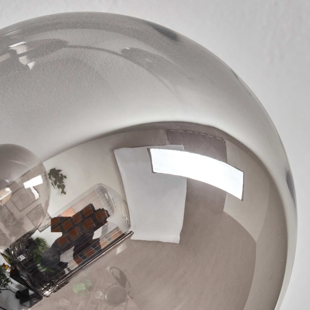 Eine glänzende, graue Glaskugel spiegelt einen Raum wider. Sichtbar sind eine Pflanze, ein klarer Plastikbehälter und weiße Wände.