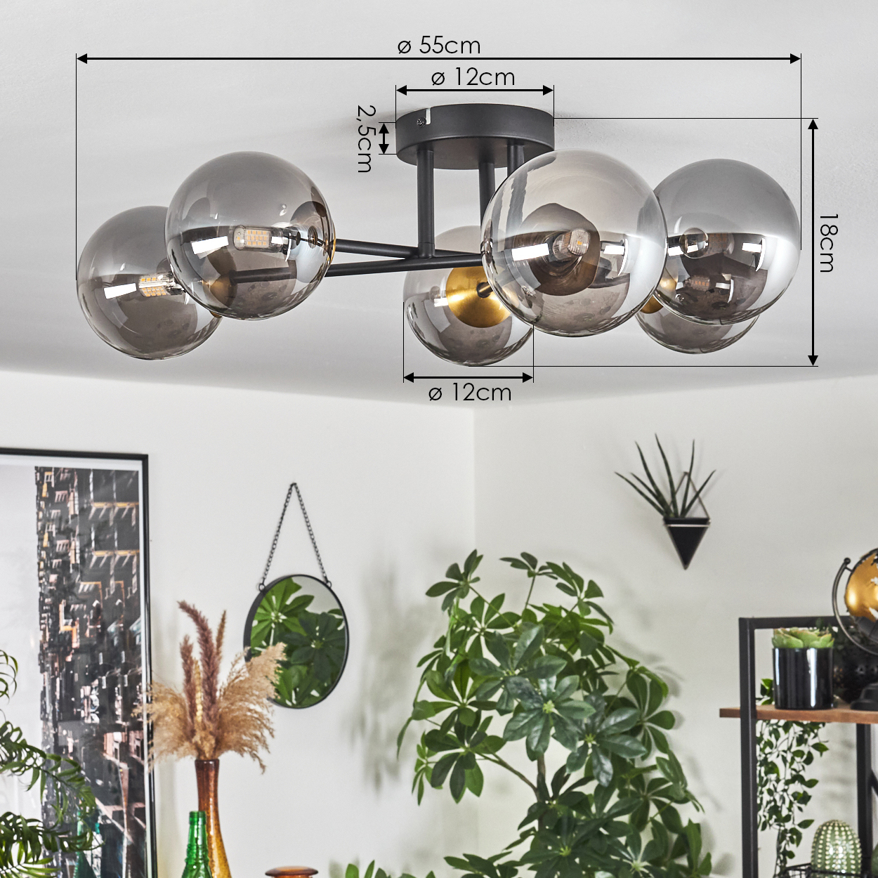 Eine moderne Deckenlampe mit fünf rauchfarbenen Glaskugeln, schwarzem Rahmen und Maßen. Pflanzen, Spiegel und Dekor sind im Hintergrund sichtbar.