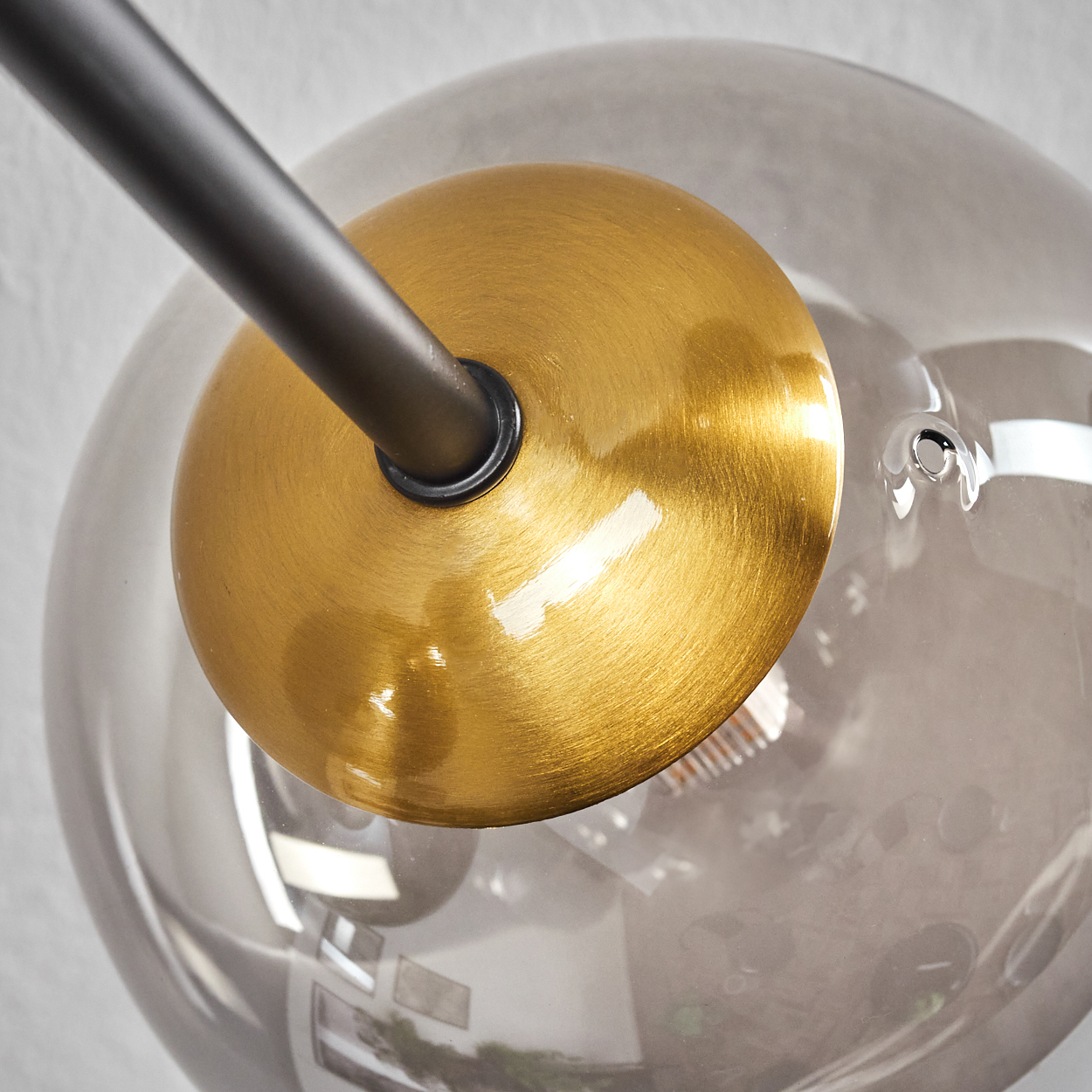 Nahaufnahme einer modernen Leuchte. Sie hat eine Messingscheibe, eine rauchige Glaskugel und einen dunklen Metallarm.