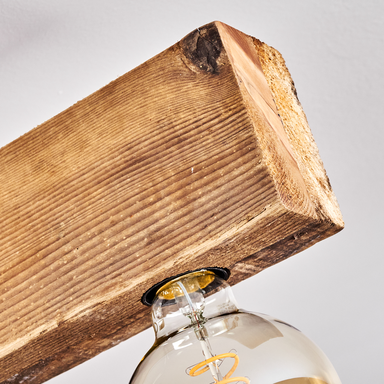 Holzbalken mit sichtbarer Maserung, der eine große Glühbirne mit sichtbarem Glühfaden trägt. Der Hintergrund ist eine schlichte weiße Wand.