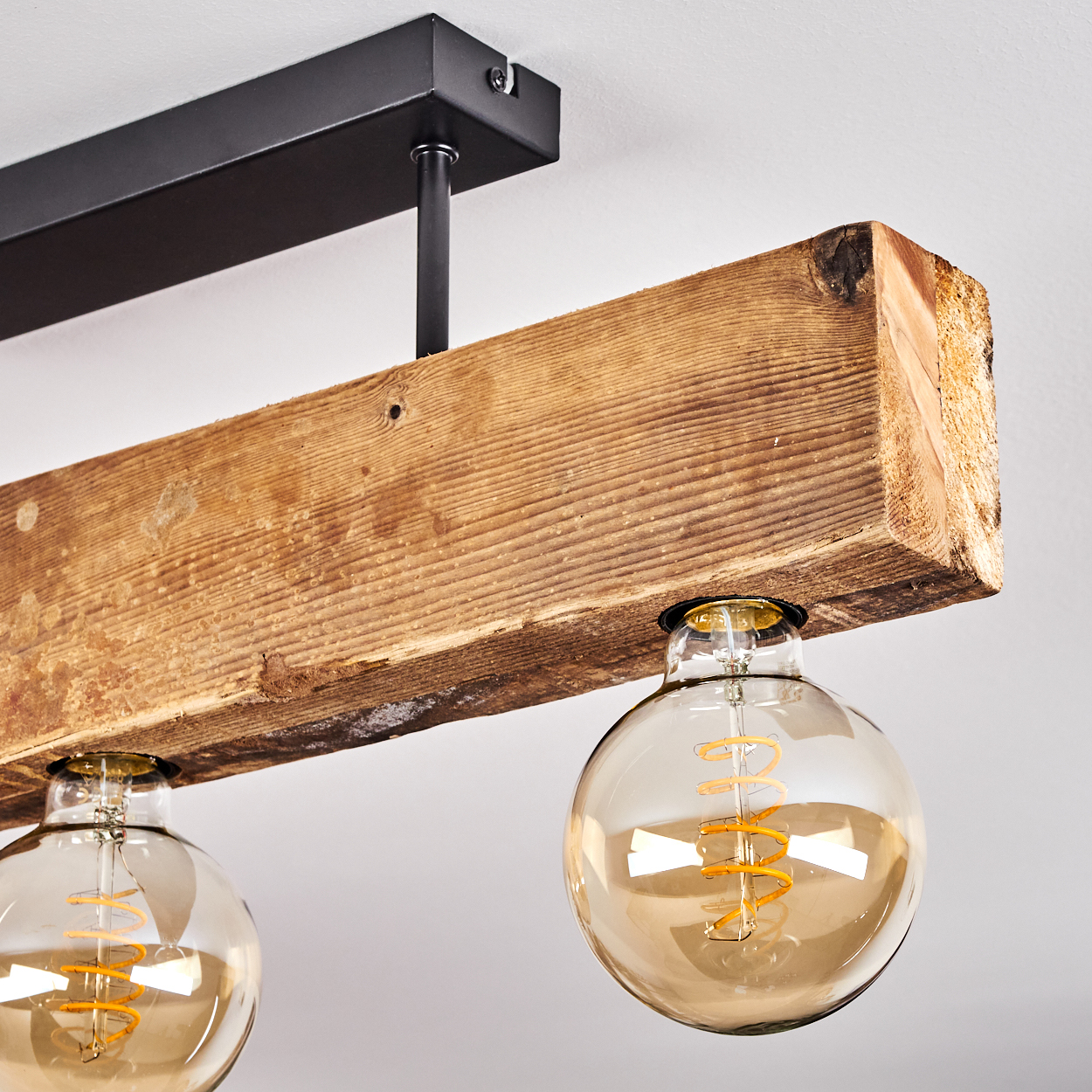 Ein Holzbalken mit zwei großen, kugelförmigen Glühbirnen. Der Balken hängt an einer schwarzen Metallhalterung.