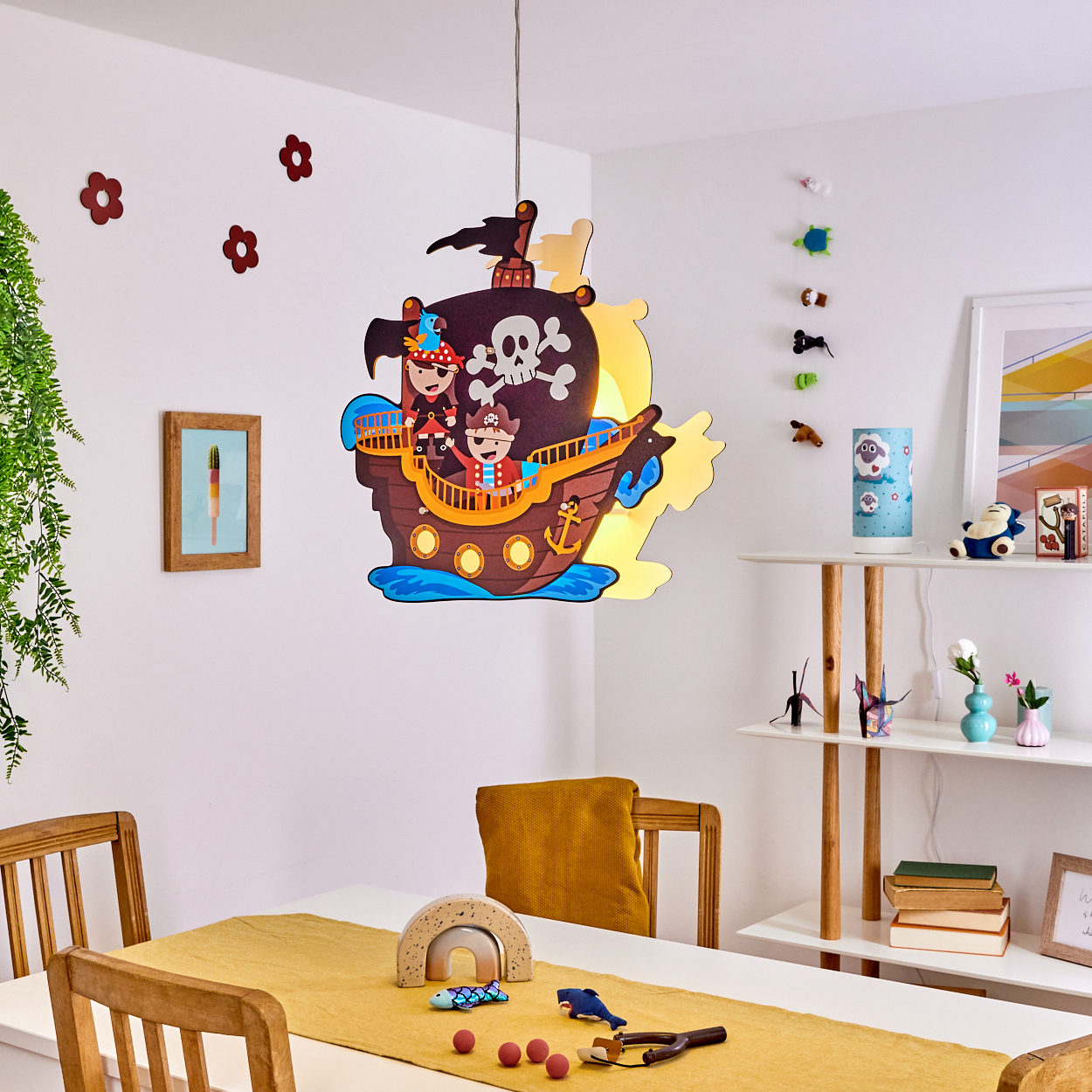 Eine Piratenschiffdekoration hängt über einem Tisch. Blumen und ein gerahmtes Bild sind an der Wand. Spielzeug liegt auf dem Tisch.