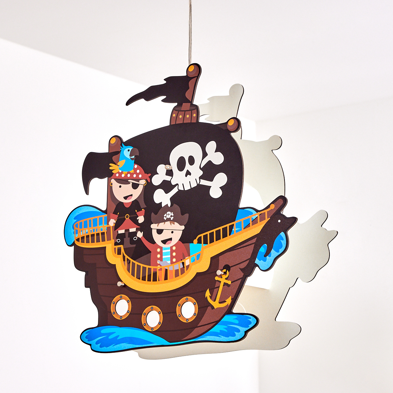 Eine Piratenschiff-Dekoration mit zwei Piraten, einem Papagei und einem Totenkopf mit gekreuzten Knochen auf dem Segel. Es hängt vor weißem Hintergrund.