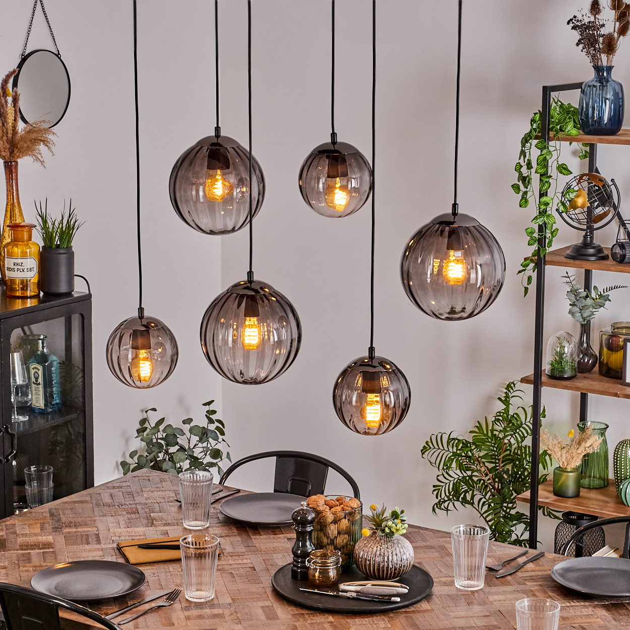 Esszimmer mit hängenden Kugelleuchten, einem Holztisch zum Abendessen und einem Bücherregal mit Dekorationsartikeln.