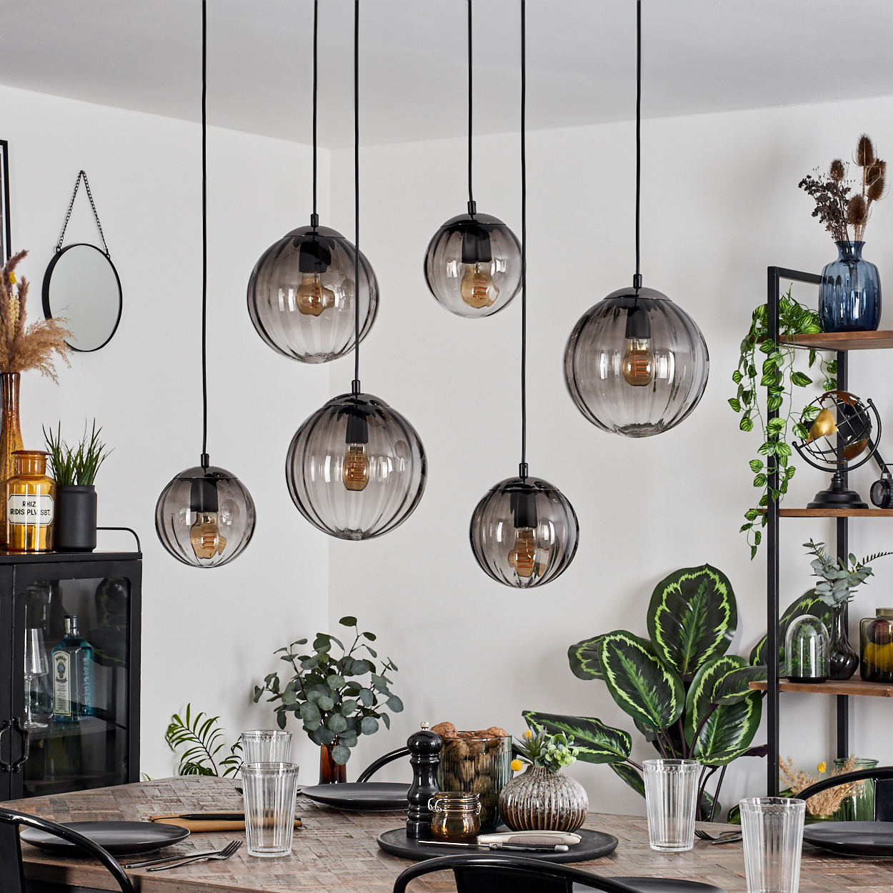 Esszimmer mit sechs Pendelleuchten, einem Holztisch für das Abendessen und Dekorationsgegenständen auf Regalen und dem Tisch.
