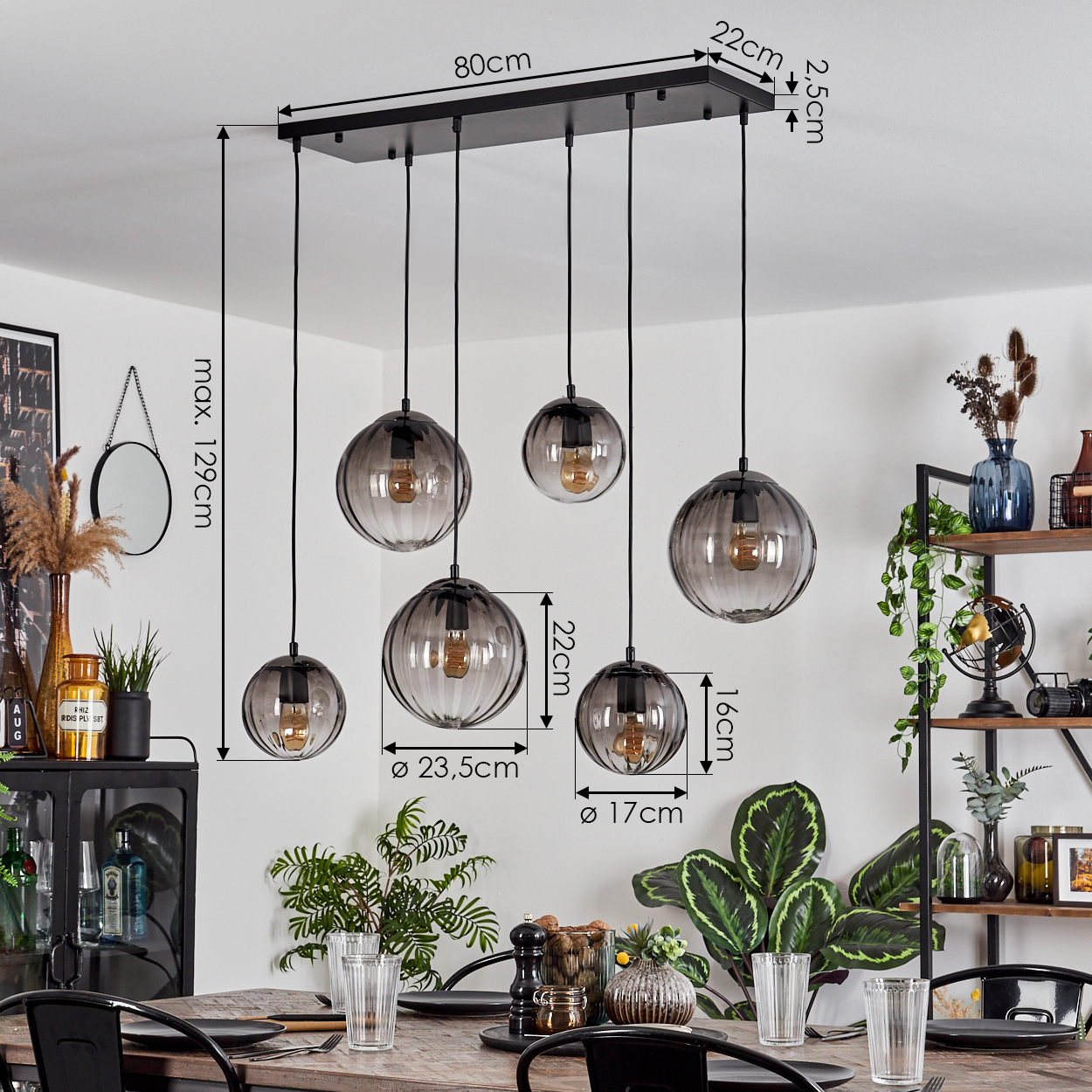 Ein modernes Esszimmer mit einer schwarzen Leuchte mit 5 Glaskugelanhängern. Ein Holztisch ist mit Gläsern und Tellern gedeckt.