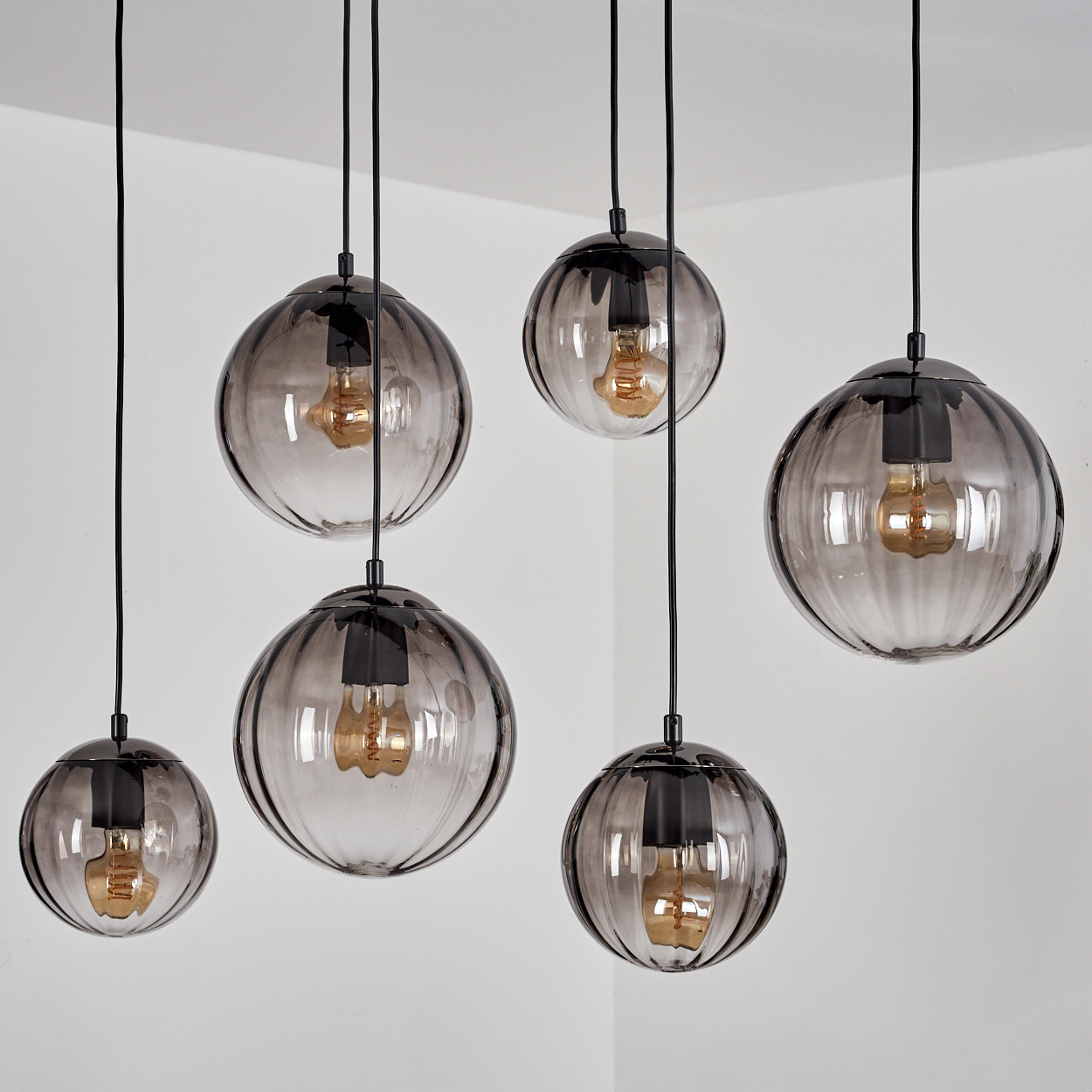 Sechs kugelförmige Pendelleuchten mit rauchgrauen Glasschirmen hängen von der Decke. Jede hat eine sichtbare Glühbirne und schwarze Armaturen.