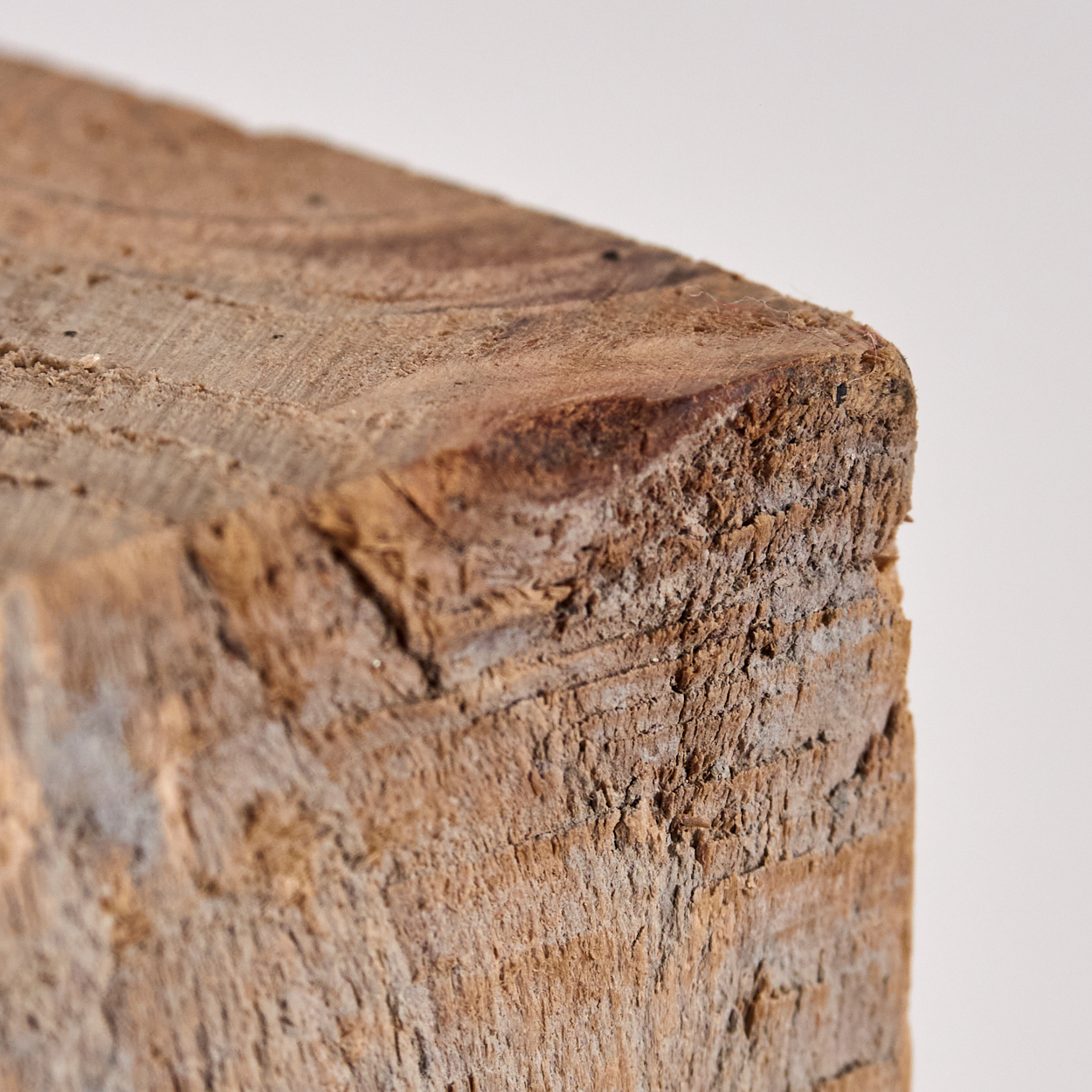 Nahaufnahme eines Holzblocks. Der Block ist braun mit sichtbarer Holzmaserung und rauer Textur. Der Hintergrund ist schlicht weiß.