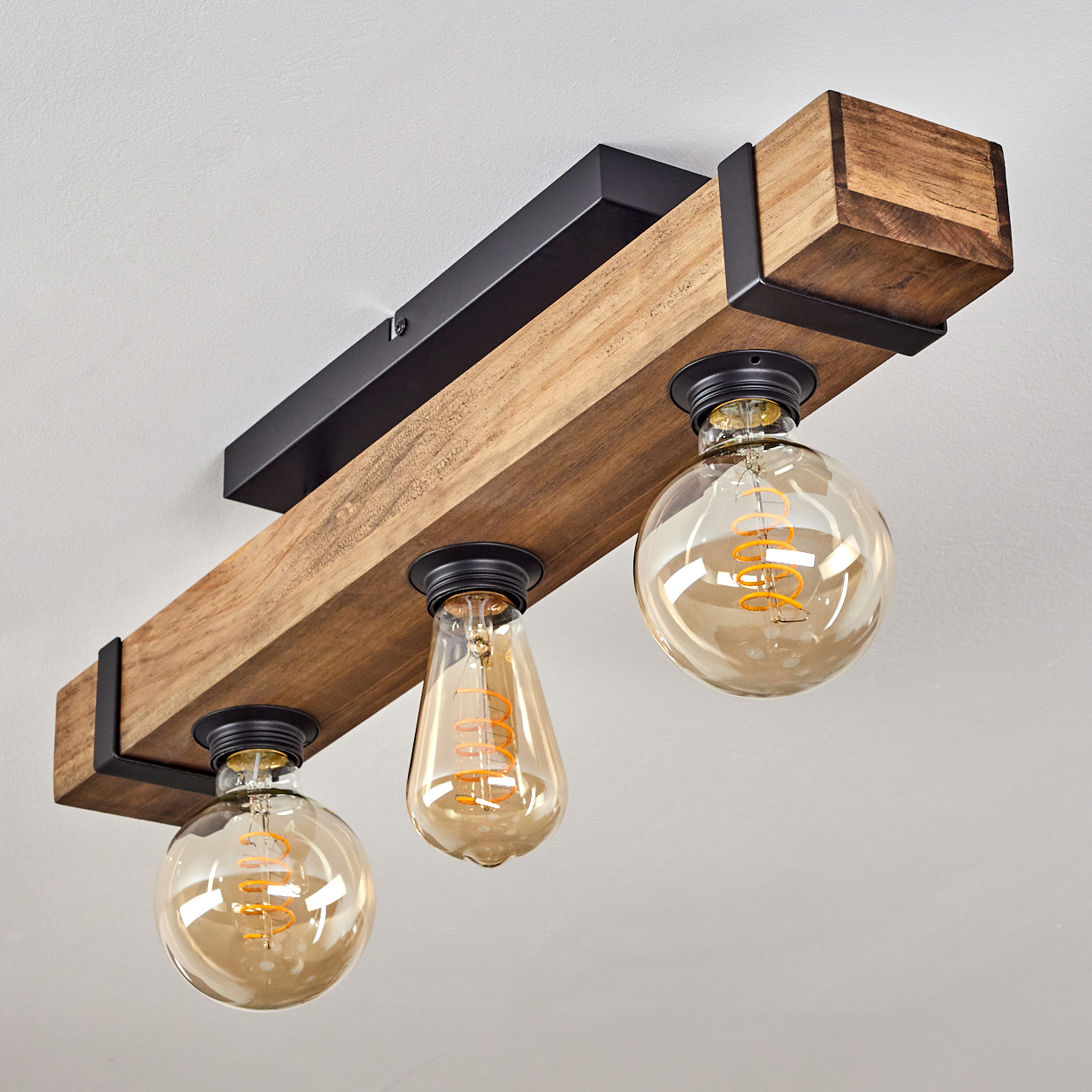 Deckenleuchte aus Holzbalken mit drei Glühbirnen. Die Glühbirnen haben verschiedene Formen und orangefarbene Glühfäden.