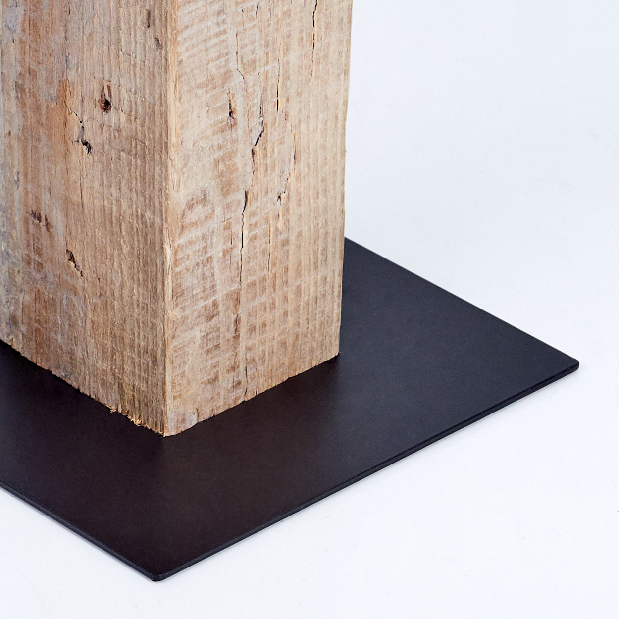 Ein verwitterter Holzbalken ruht auf einer schwarzen Metallplatte vor weißem Hintergrund. Das Holz ist strukturiert und hellbraun.