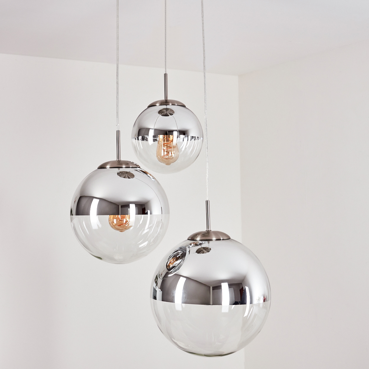 Drei verchromte und gläserne Pendelleuchten hängen von der Decke. Jede hat eine sichtbare Glühbirne.