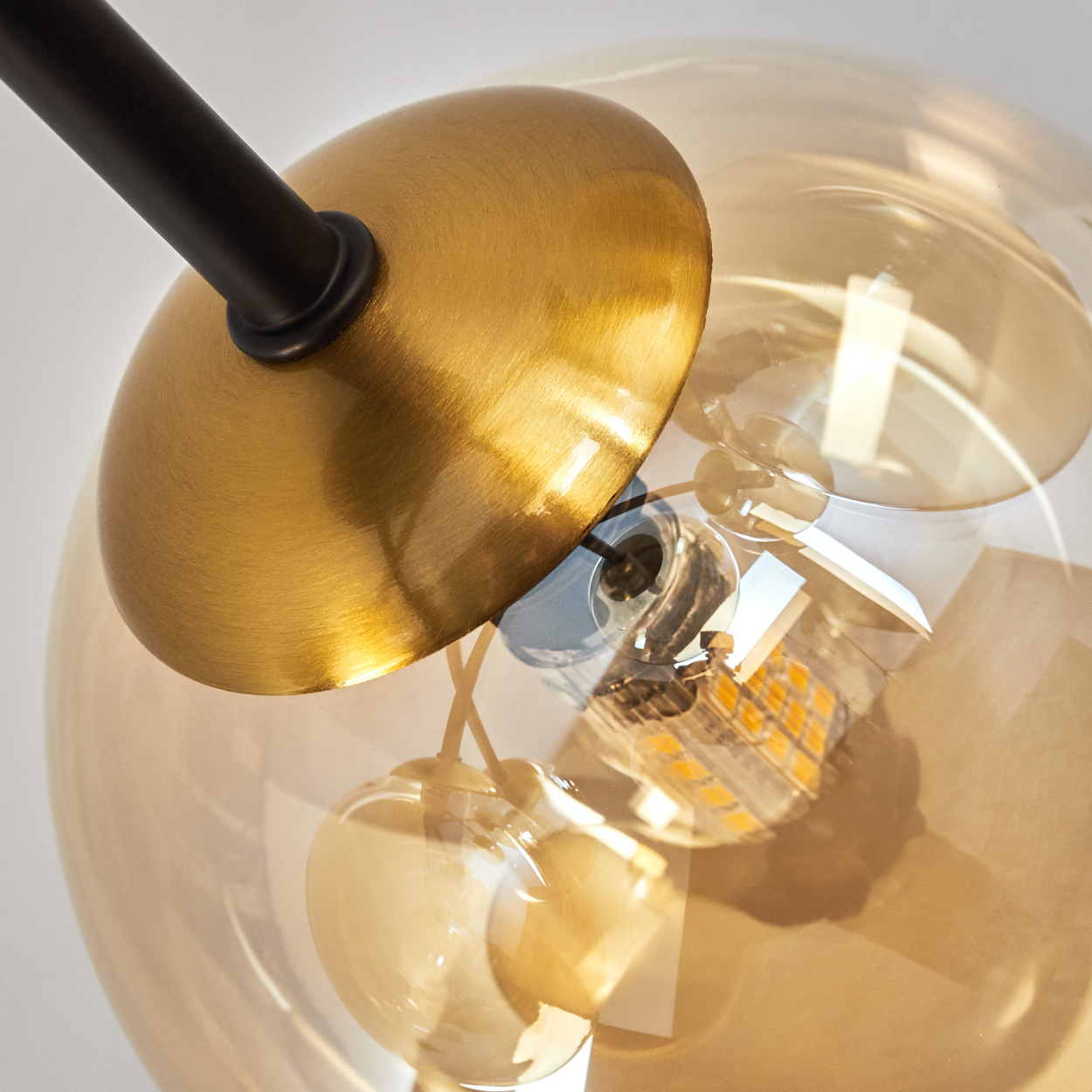 Nahaufnahme einer modernen Lampe. Sie hat eine goldfarbene Platte, einen schwarzen Stiel und einen transparenten, kugelförmigen Glasschirm mit Glühbirne.