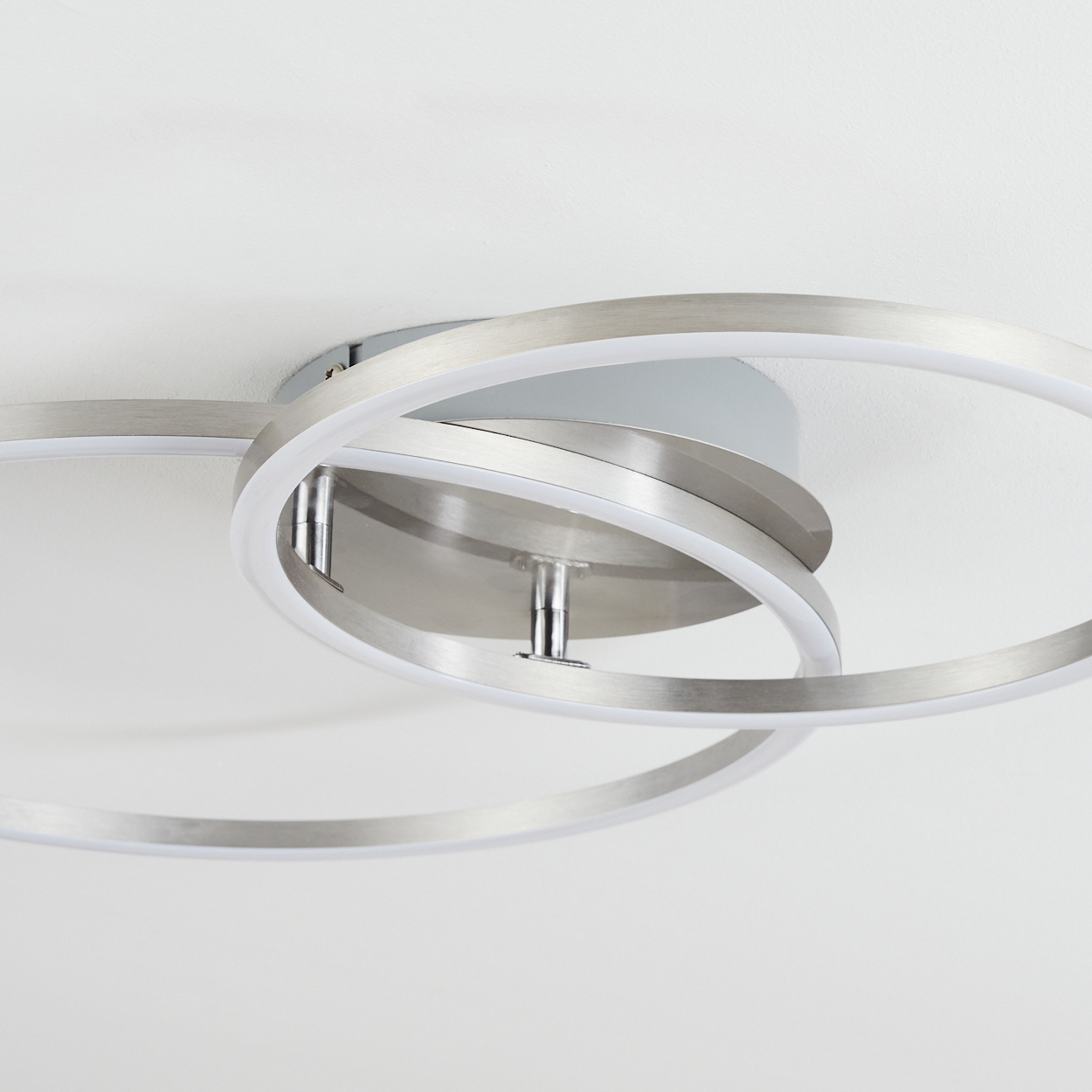 Eine moderne Deckenleuchte mit drei sich überlappenden silbernen Ringen und weißen LED-Streifen, montiert an einer weißen Decke.