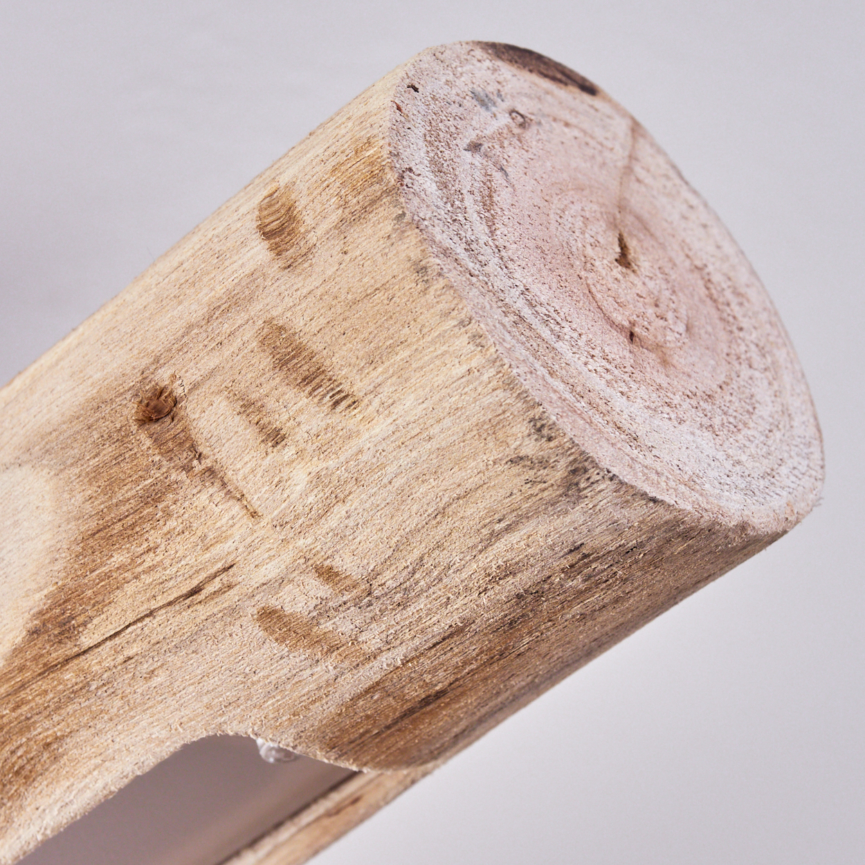 Nahaufnahme eines Holzscheits. Das Ende zeigt Jahresringe. Der Stamm ist hellbraun mit strukturierter Rinde und neutralgrauem Hintergrund.