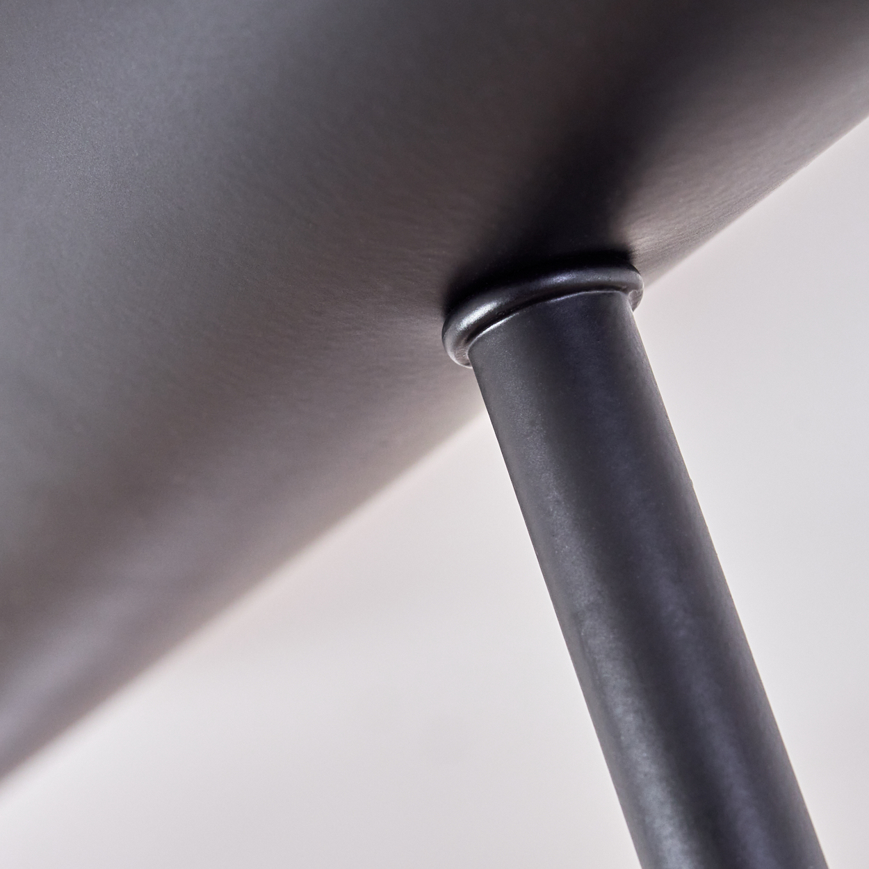 Nahaufnahme einer schwarzen Metallkonstruktion, möglicherweise ein Tisch. Ein zylindrisches Bein verbindet sich mit einer flachen Oberfläche, vor weißem Hintergrund.