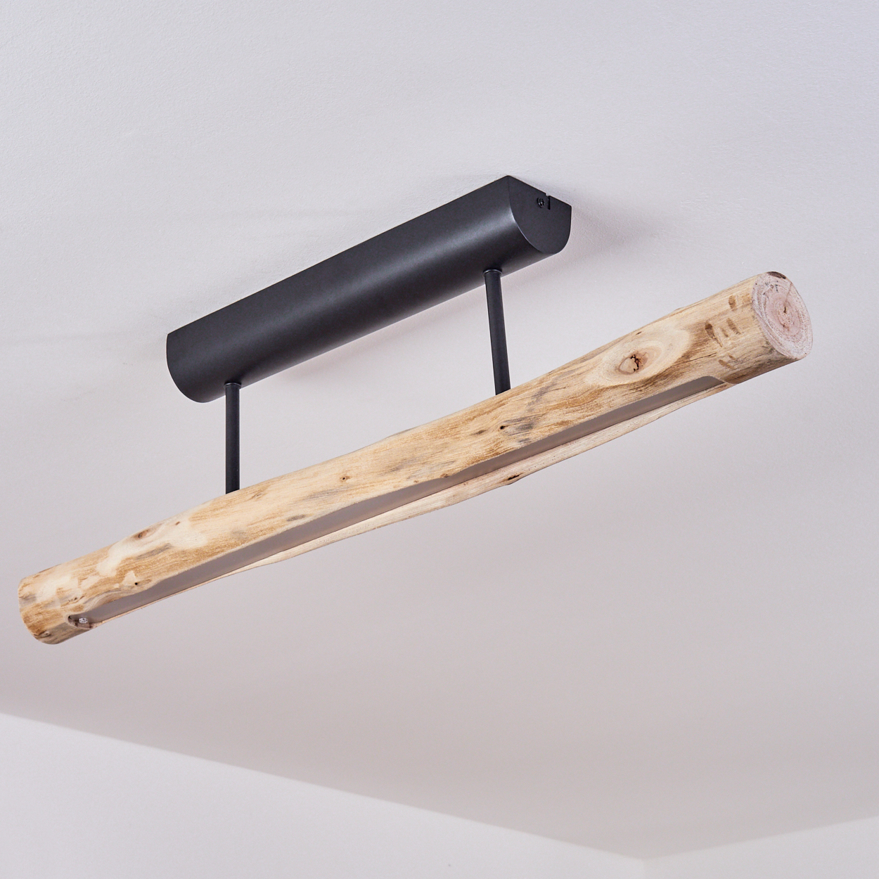 Eine moderne Leuchte. Sie hat eine schwarze Metalloberseite und eine Holzträgerbasis, die von der Decke hängt. Der Hintergrund ist weiß.