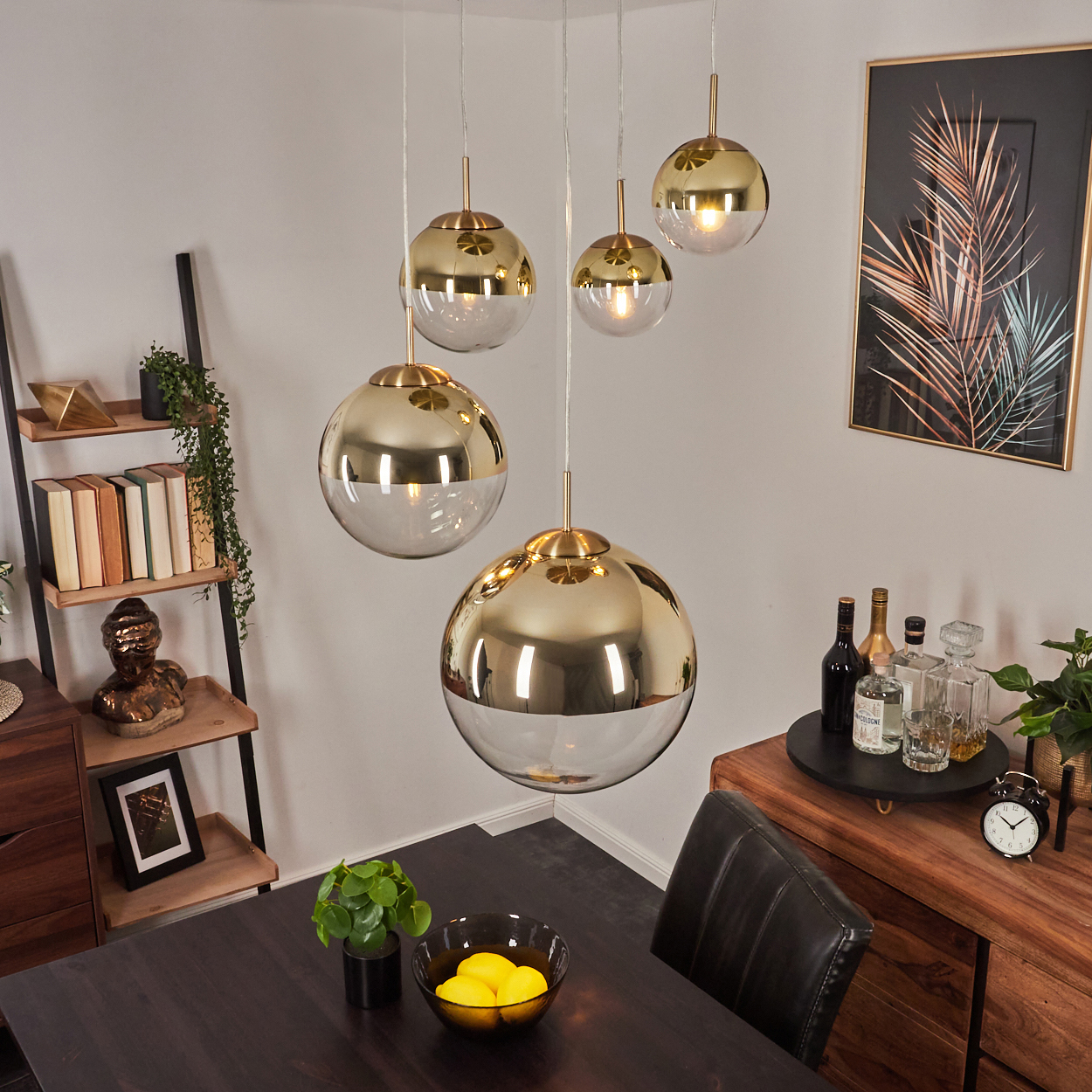 Ein Esszimmer mit hängenden Gold- und Glasleuchten. Ein Tisch mit Zitronen, ein Servierwagen und ein gerahmtes Bild sind ebenfalls zu sehen.