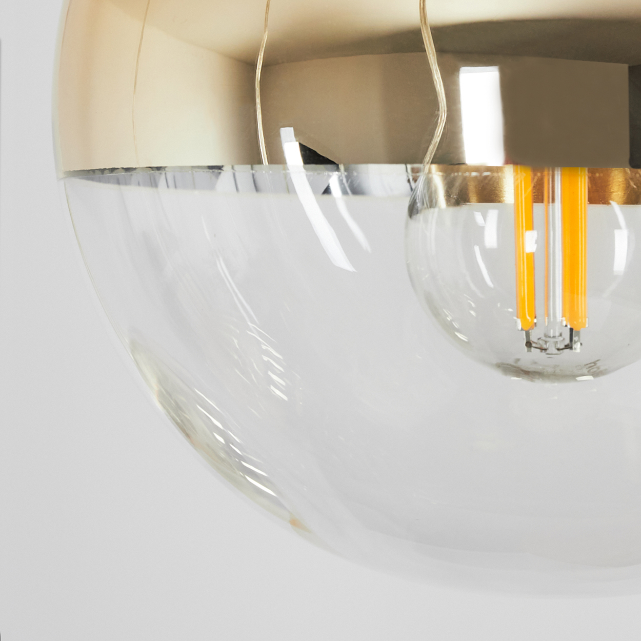 Nahaufnahme einer klaren Glaskugel-Leuchte mit goldenem Deckel und einer orangefarbenen Glühbirne.