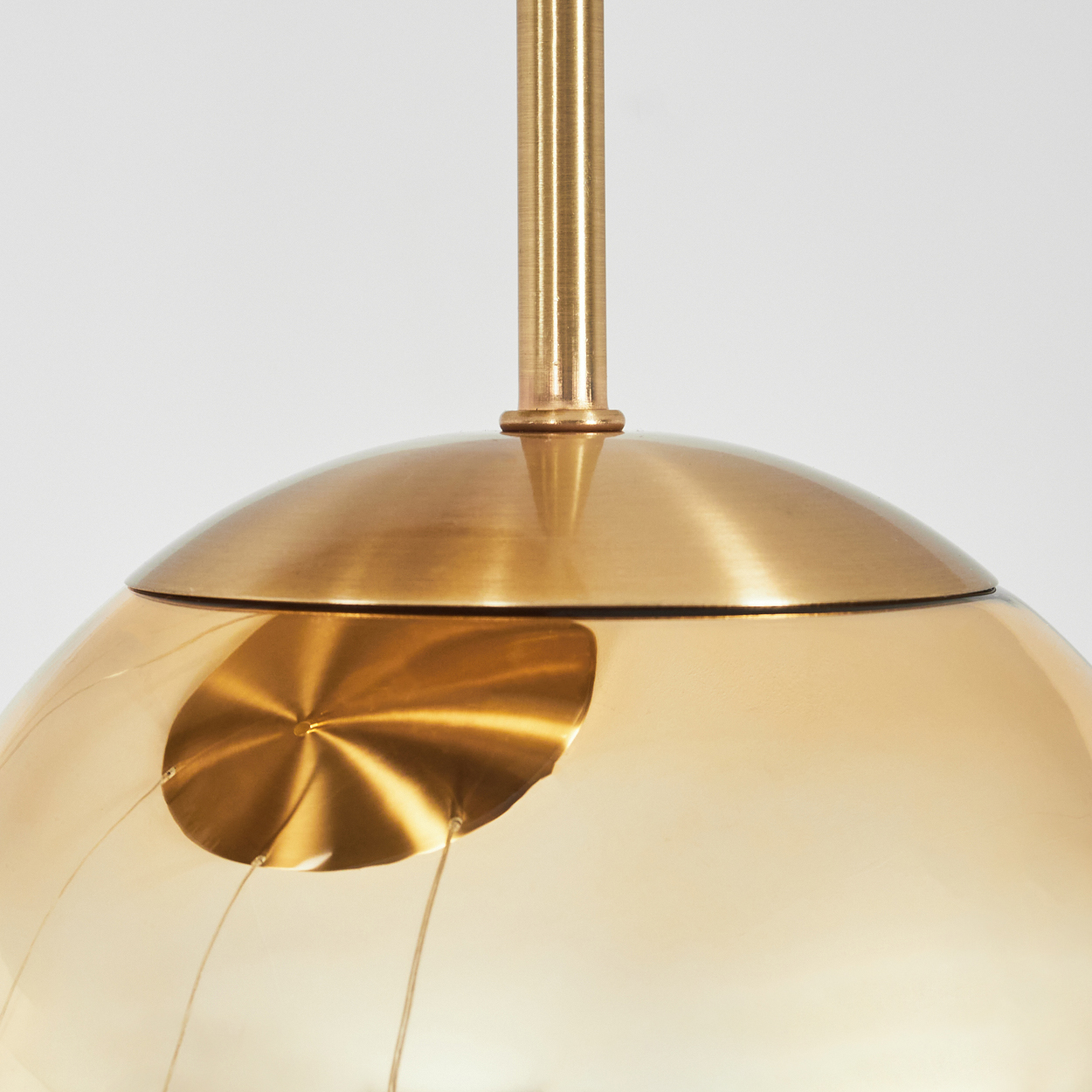 Nahaufnahme einer goldfarbenen Pendelleuchte. Die Lampe hat einen abgerundeten Schirm und eine vertikale Stange. Der Hintergrund ist weiß.