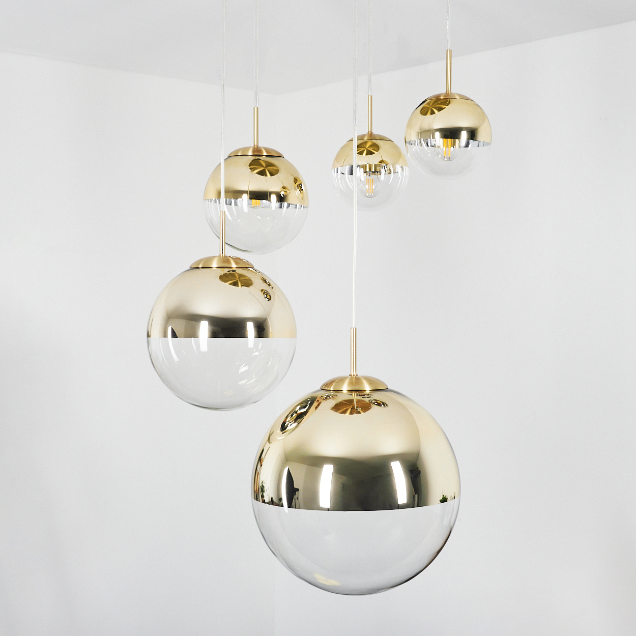 Fünf gold- und glaskugelförmige Pendelleuchten, die von der Decke hängen. Die obere Hälfte ist gold, die untere Hälfte klar.