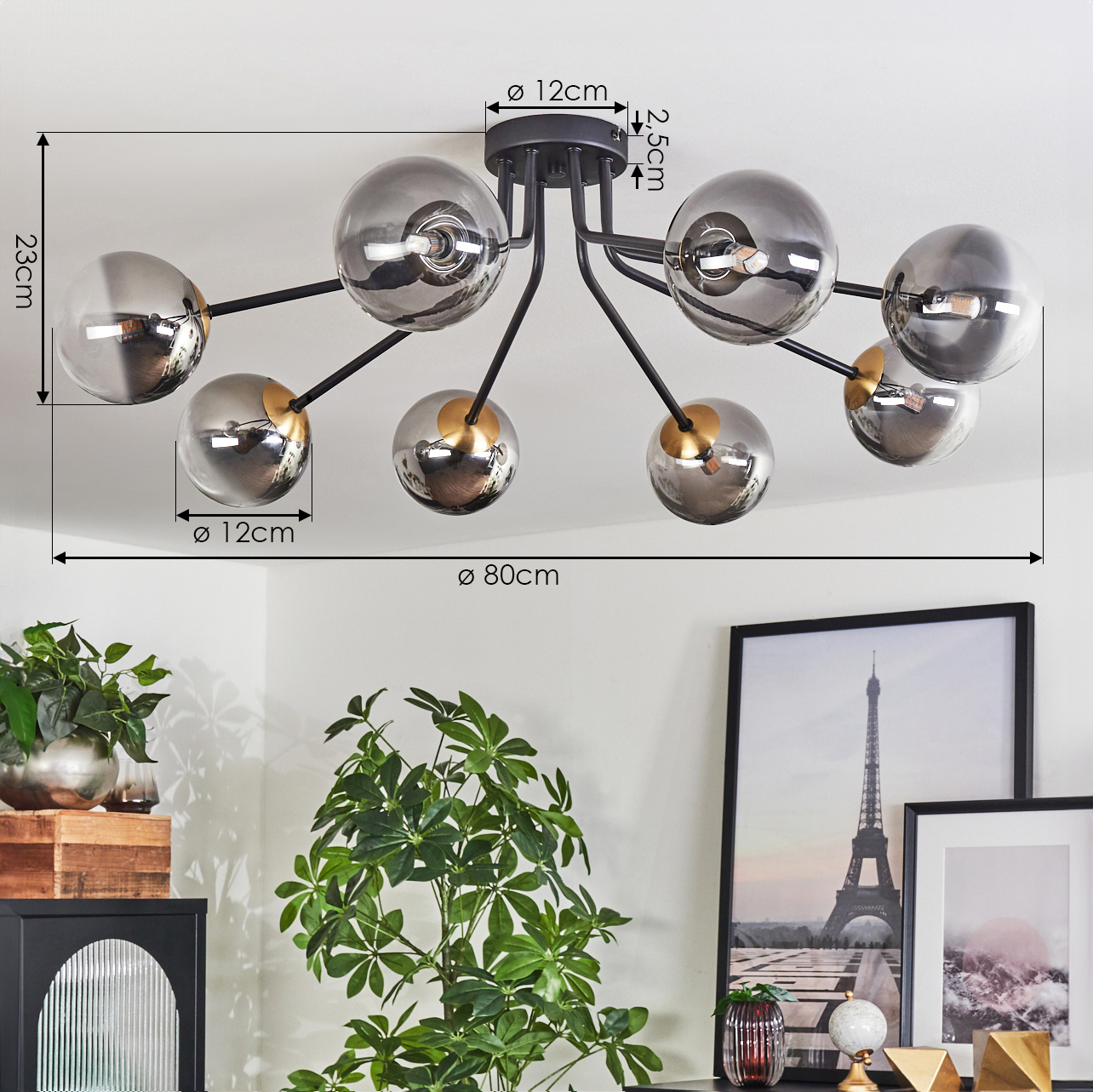 Eine moderne Deckenlampe mit kugelförmigen Lichtern hängt von der Decke. Darunter befinden sich Pflanzen, gerahmte Kunst und Dekorationsgegenstände.