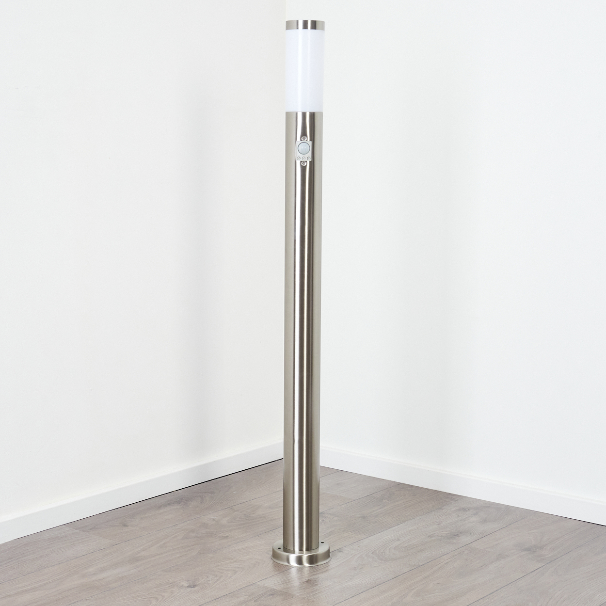 Eine hohe, silberne Laterne steht auf einem Holzboden vor einer weißen Wand. Die Lampe hat einen weißen Kopf und Steuertasten.