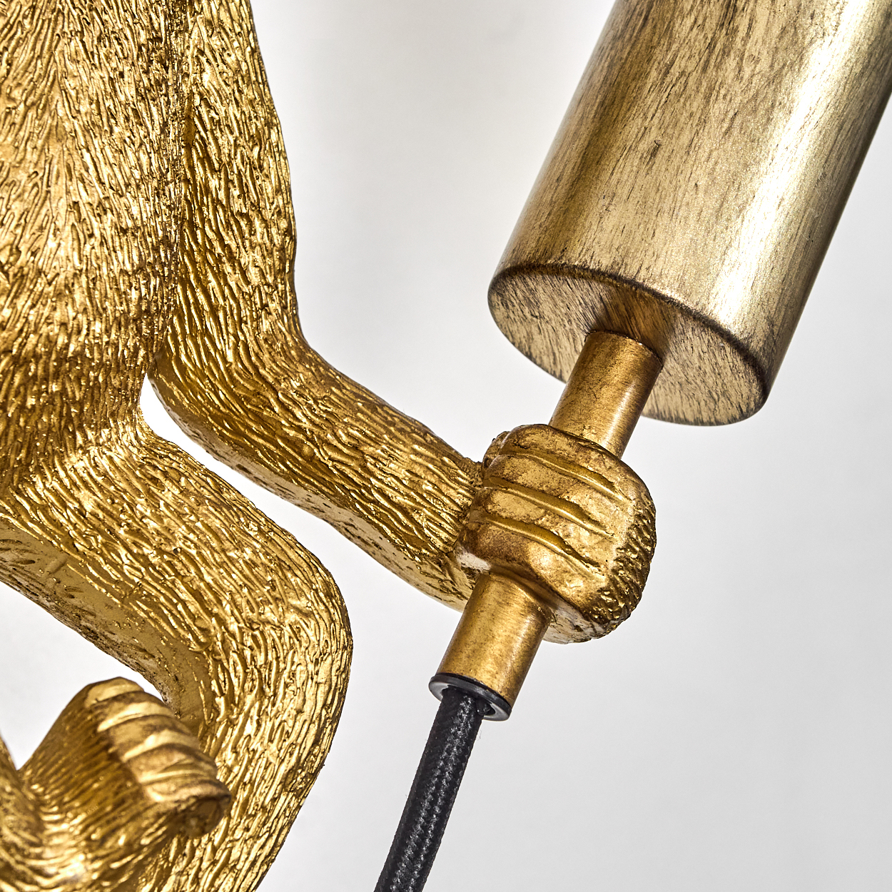 Eine goldene Affenstatue, die eine goldene Lampe hält. Der Affe ist detailliert, und die Lampe hat ein schwarzes Kabel. Der Hintergrund ist weiß.
