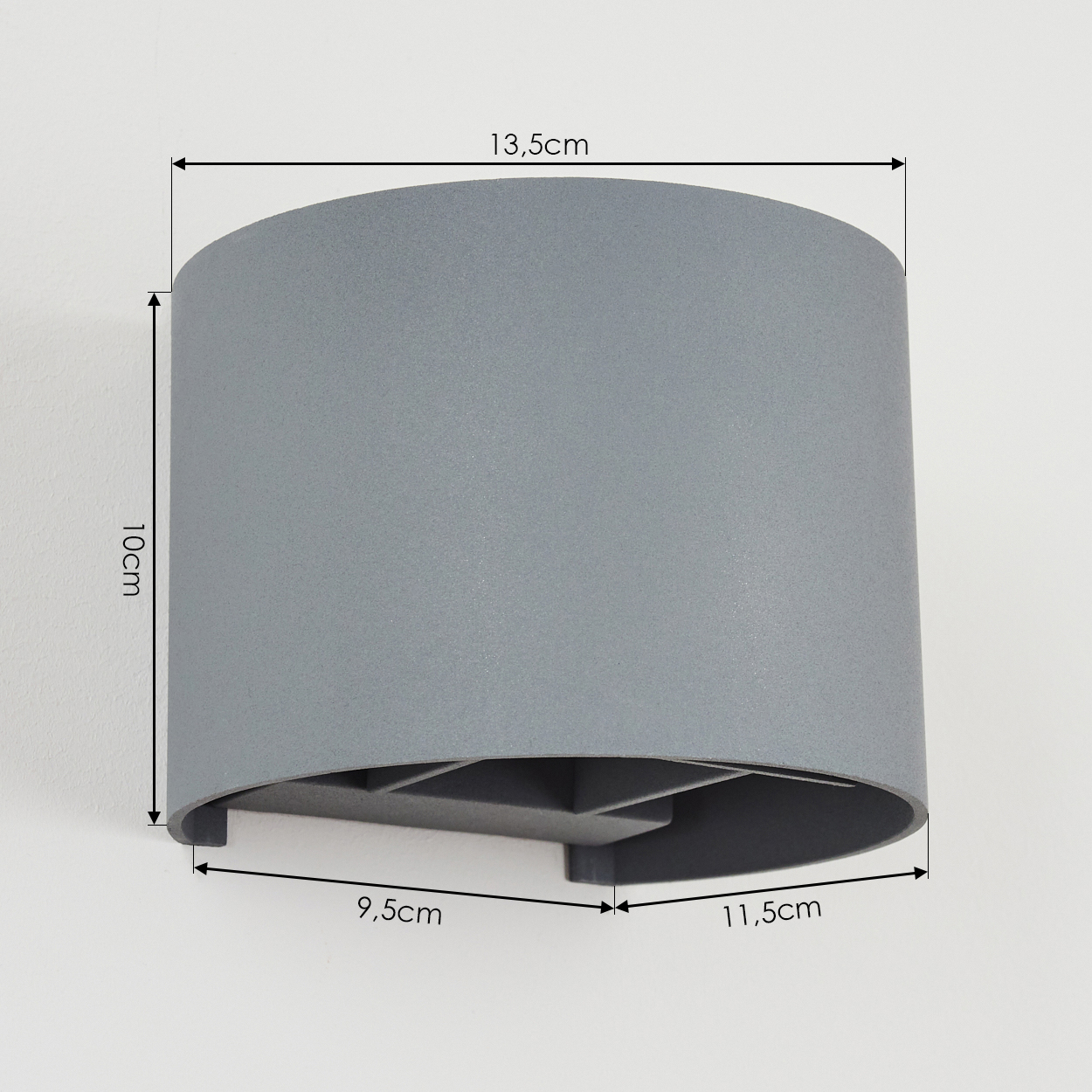 Eine graue, halb zylindrische Wandleuchte ist an einer weißen Wand montiert. Abmessungen: 13,5 cm breit, 10 cm hoch, Sockel 9,5 cm und 11,5 cm.
