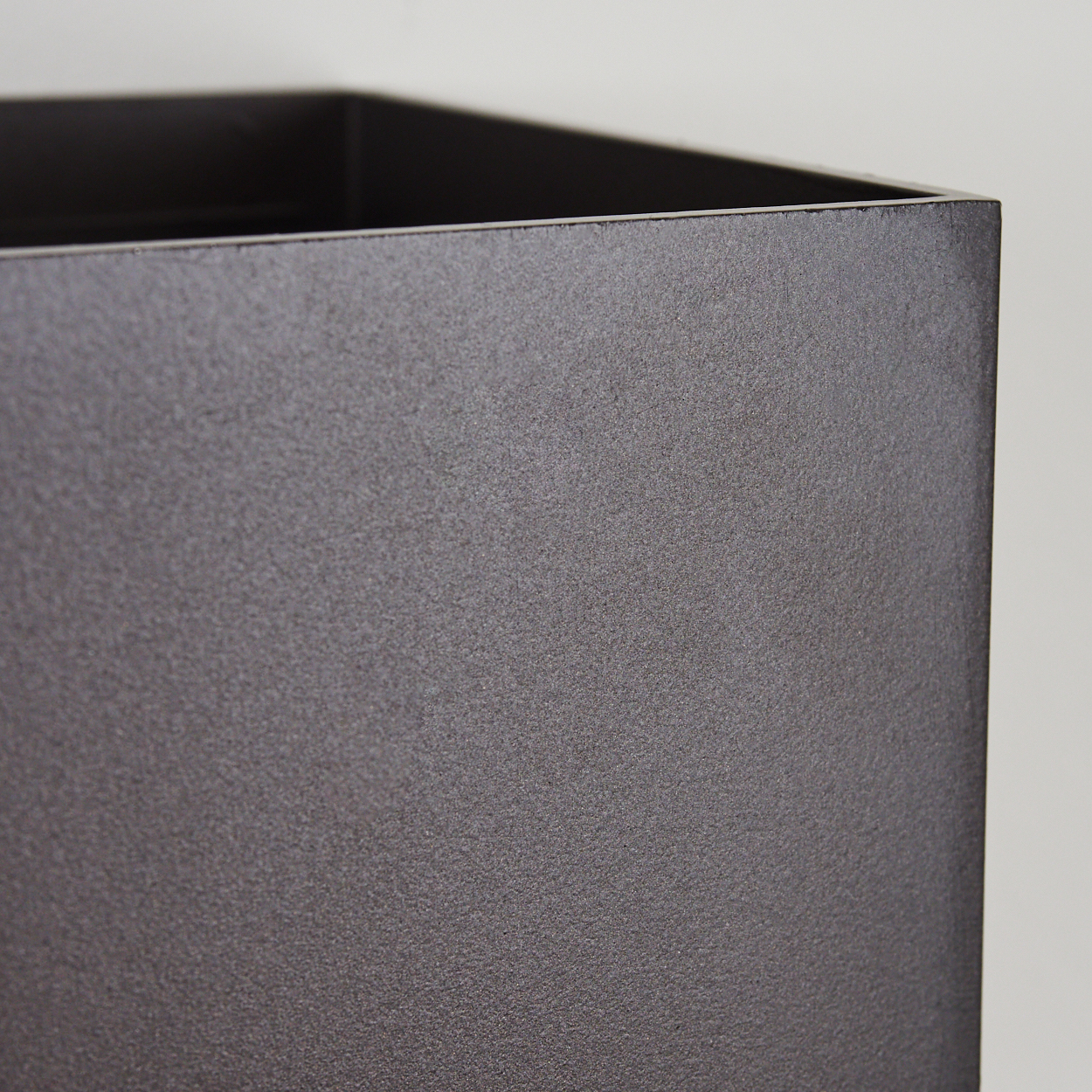 Nahaufnahme einer dunklen, strukturierten Boxecke. Die Box ist matt, dunkelgrau. Der Hintergrund ist eine schlichte, hellgraue Oberfläche.