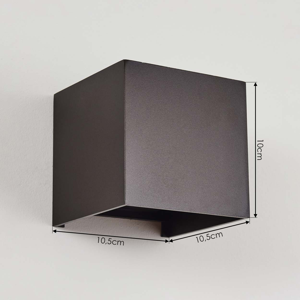 Dunkelbraune, quadratische Wandleuchte. Maße sind beschriftet: 10,5 cm, 10 cm und 10,5 cm. Sie ist an einer weißen Wand montiert.