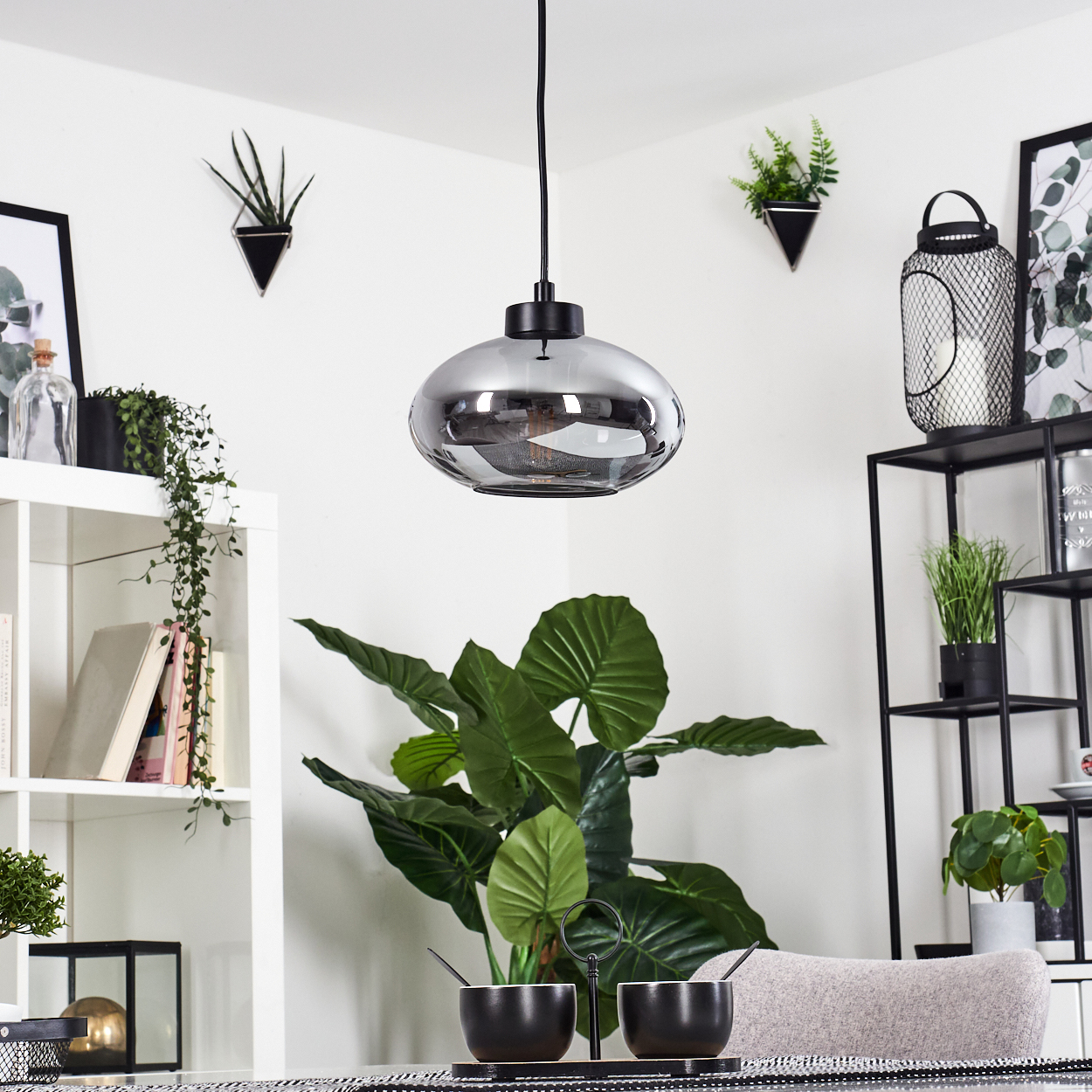 Ein modernes Esszimmer mit Glas-Pendelleuchte, Pflanzen, schwarzem Tisch und schwarzem Regal.